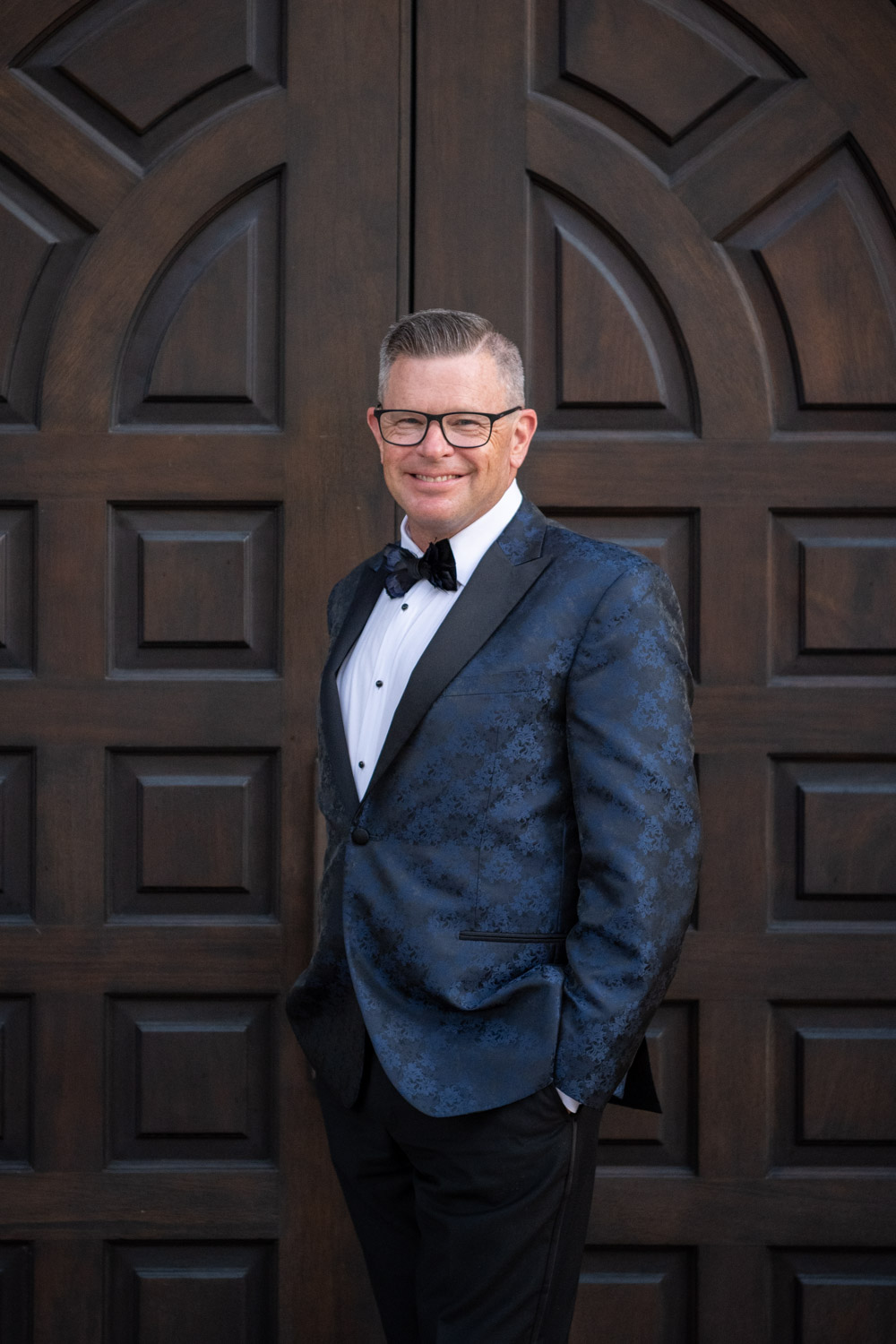 groom smiles as he looks dashing in his blue tuxedo jacket
