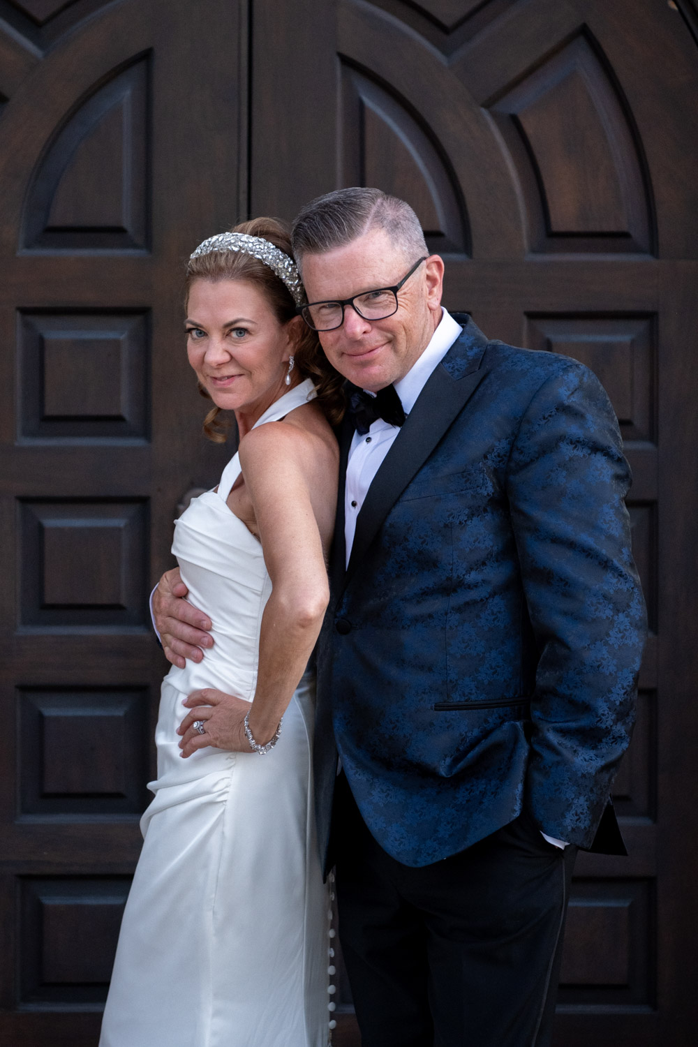 groom smiles as he wraps his arm around his smiling bride as they stand outside the door at Sage SRQ