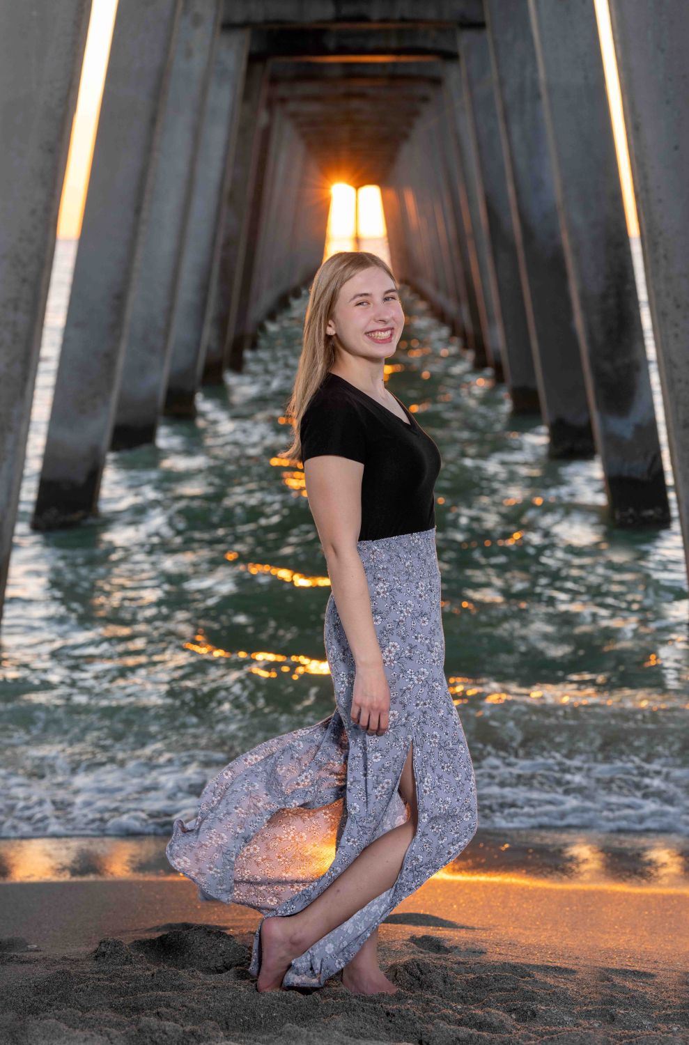 Senior photo in Venice Florida of girl in black top and flowing skirt standing under the Fishing Pier