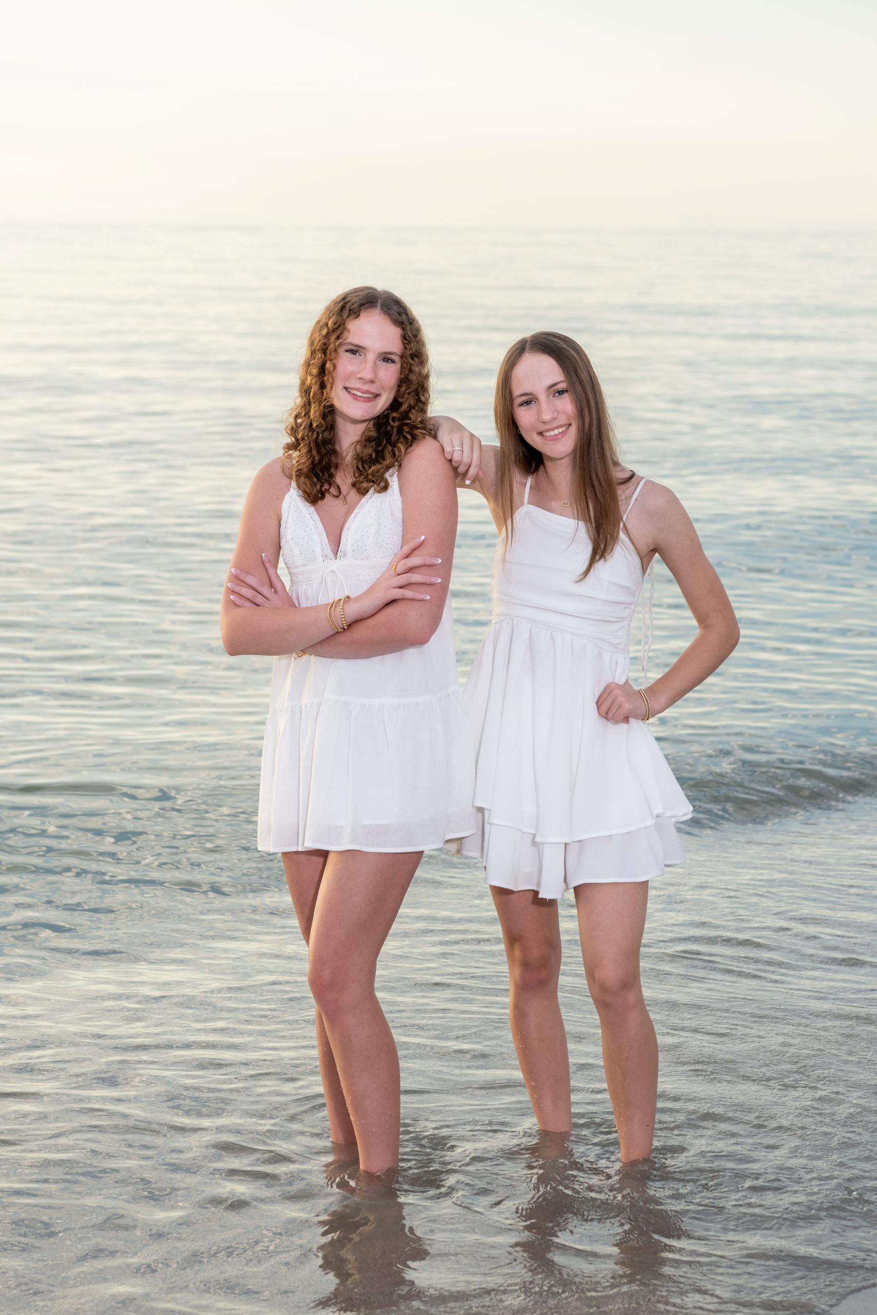 sisters in white dresses stand together in the water