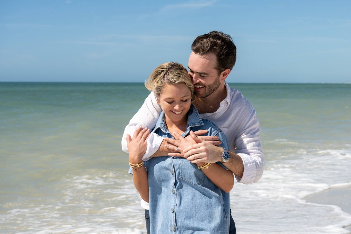 man wraps his arms around his fiance and whispers in her ear