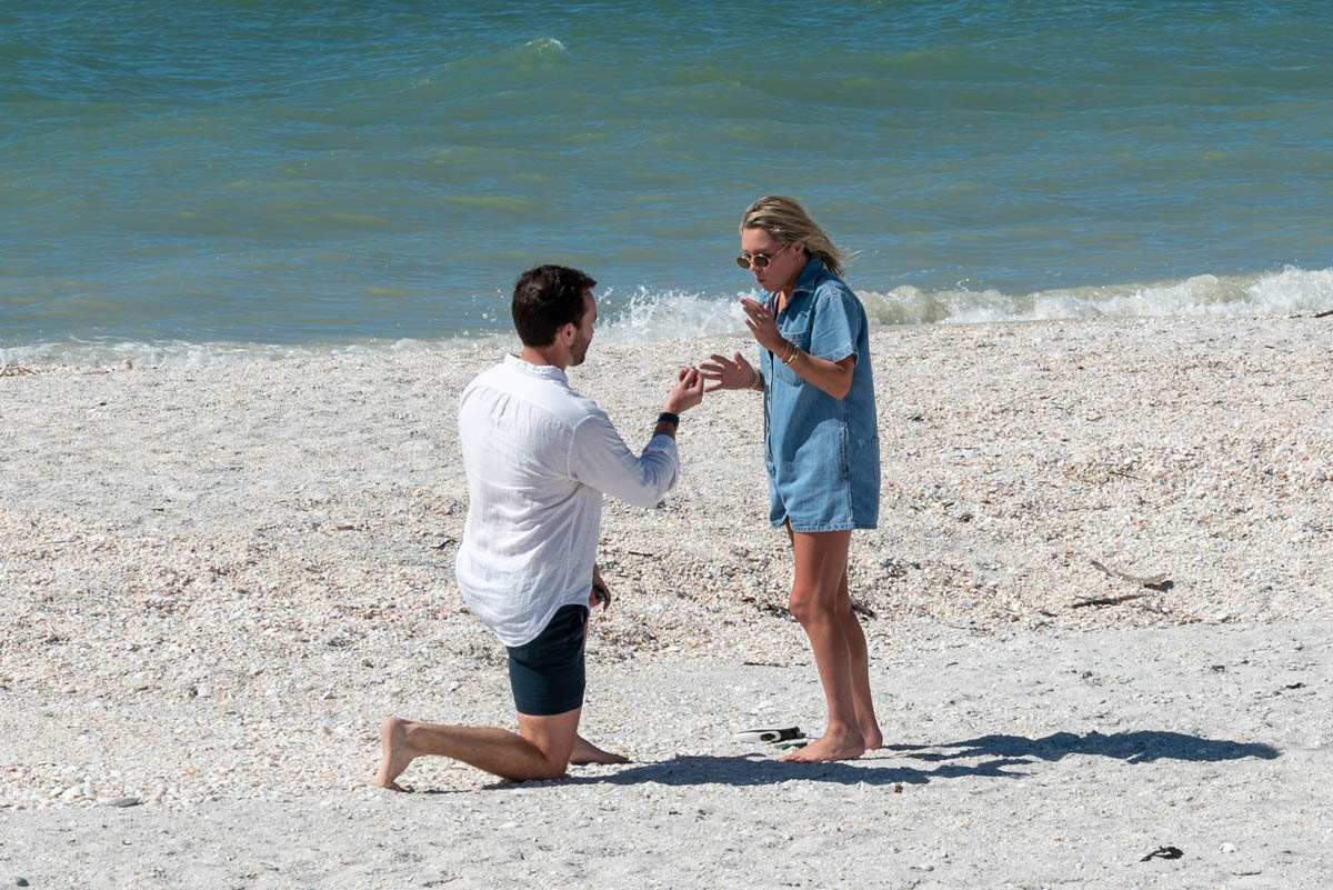 man drops down on his knee to propose on the beach