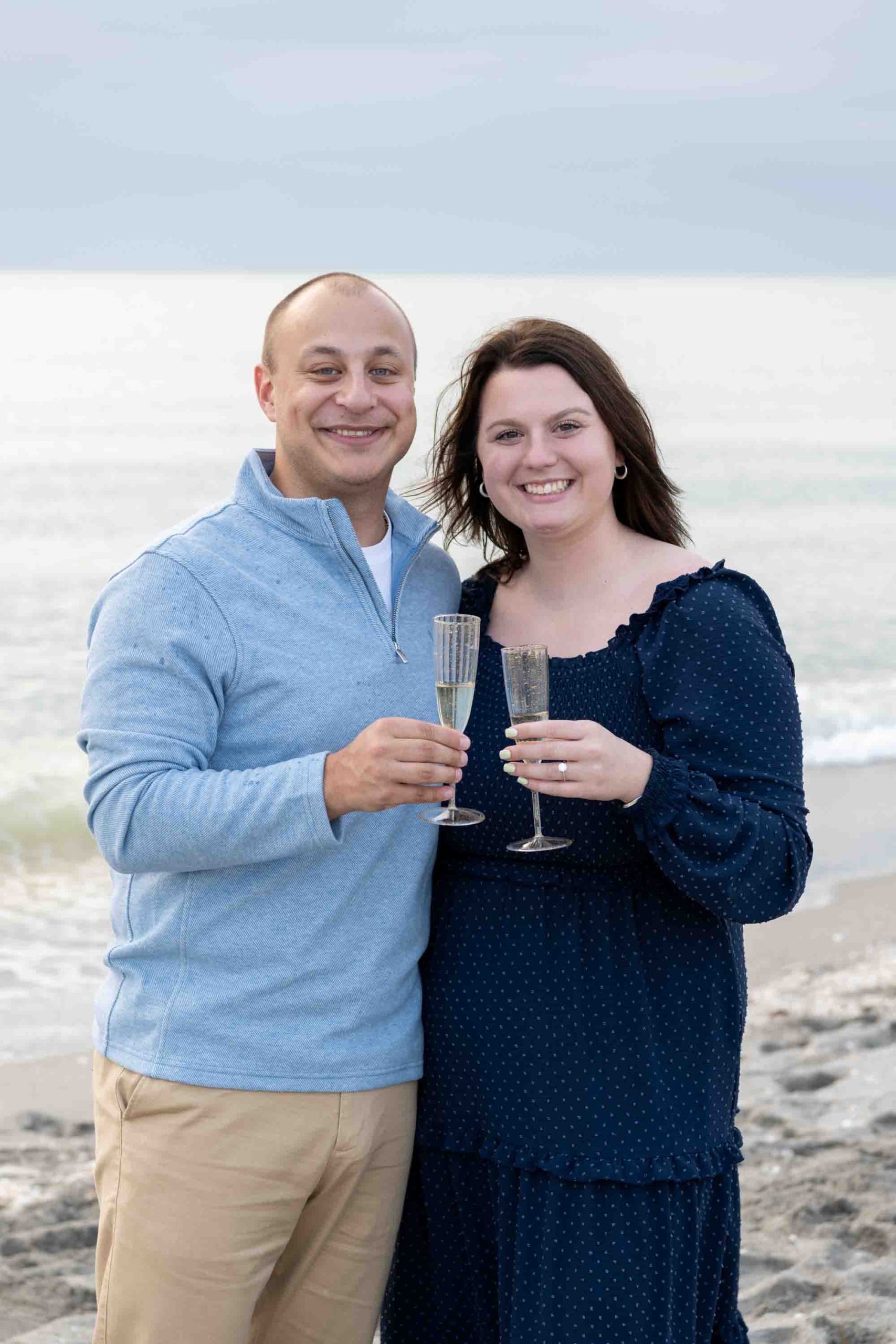 newly engaged couple smile as they hold champagne glasses