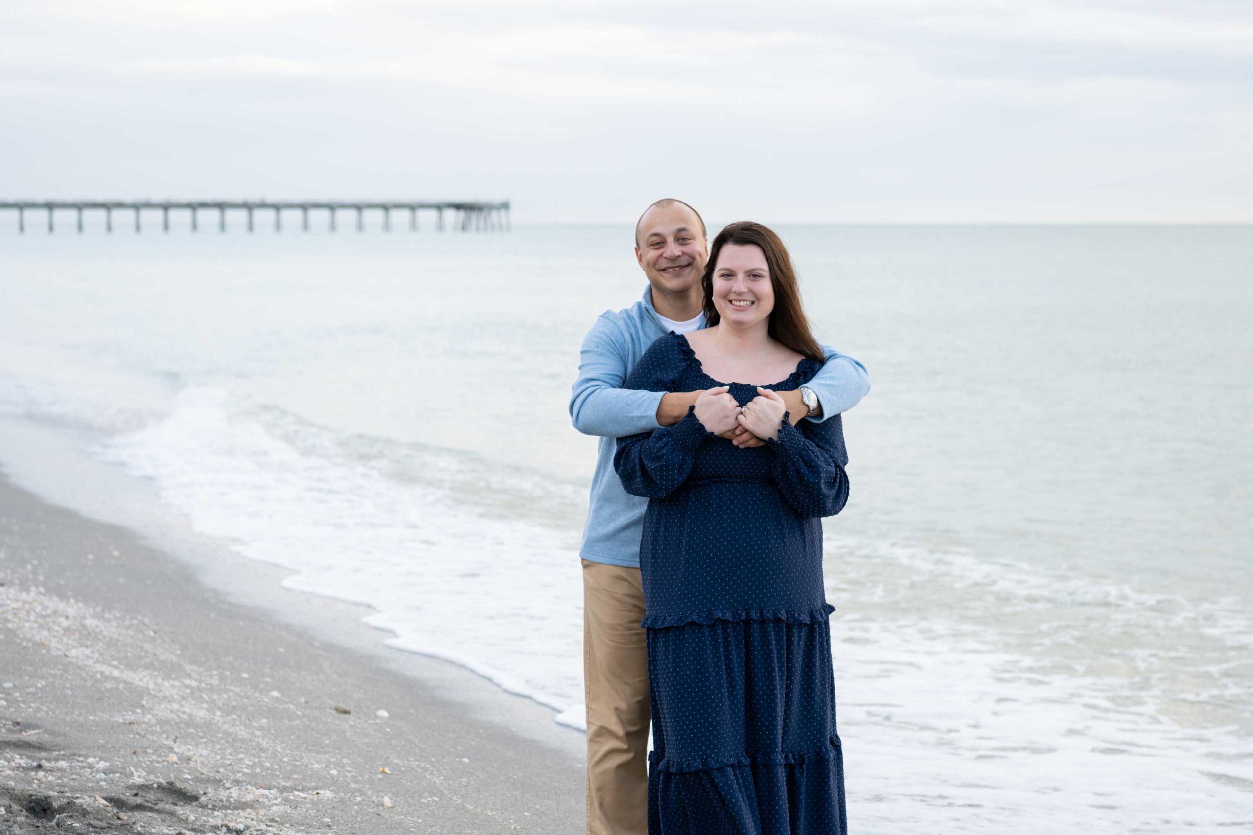 guy wraps his arms around his fiance with the Venice Fishing Pier in the background
