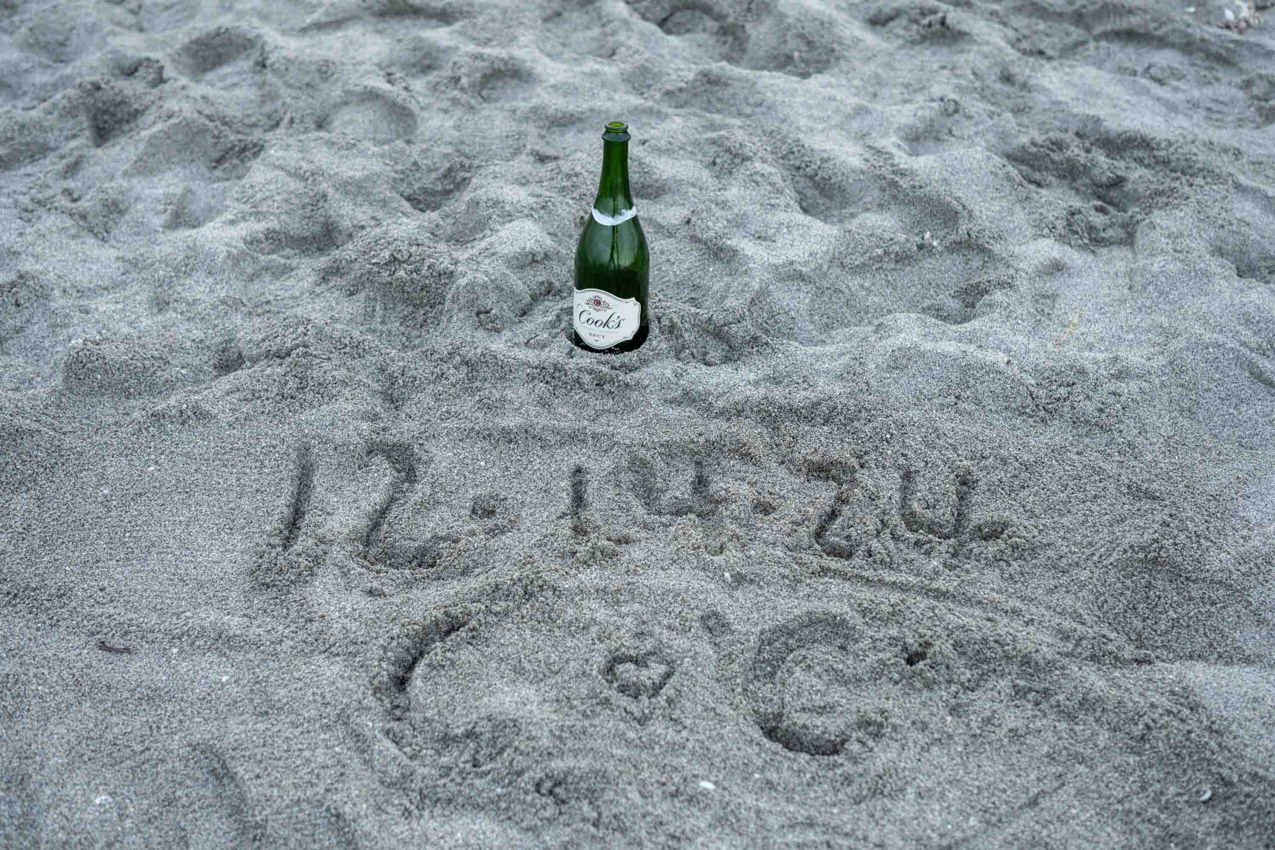 bottle of champagne in the sand and the date of the engagement written