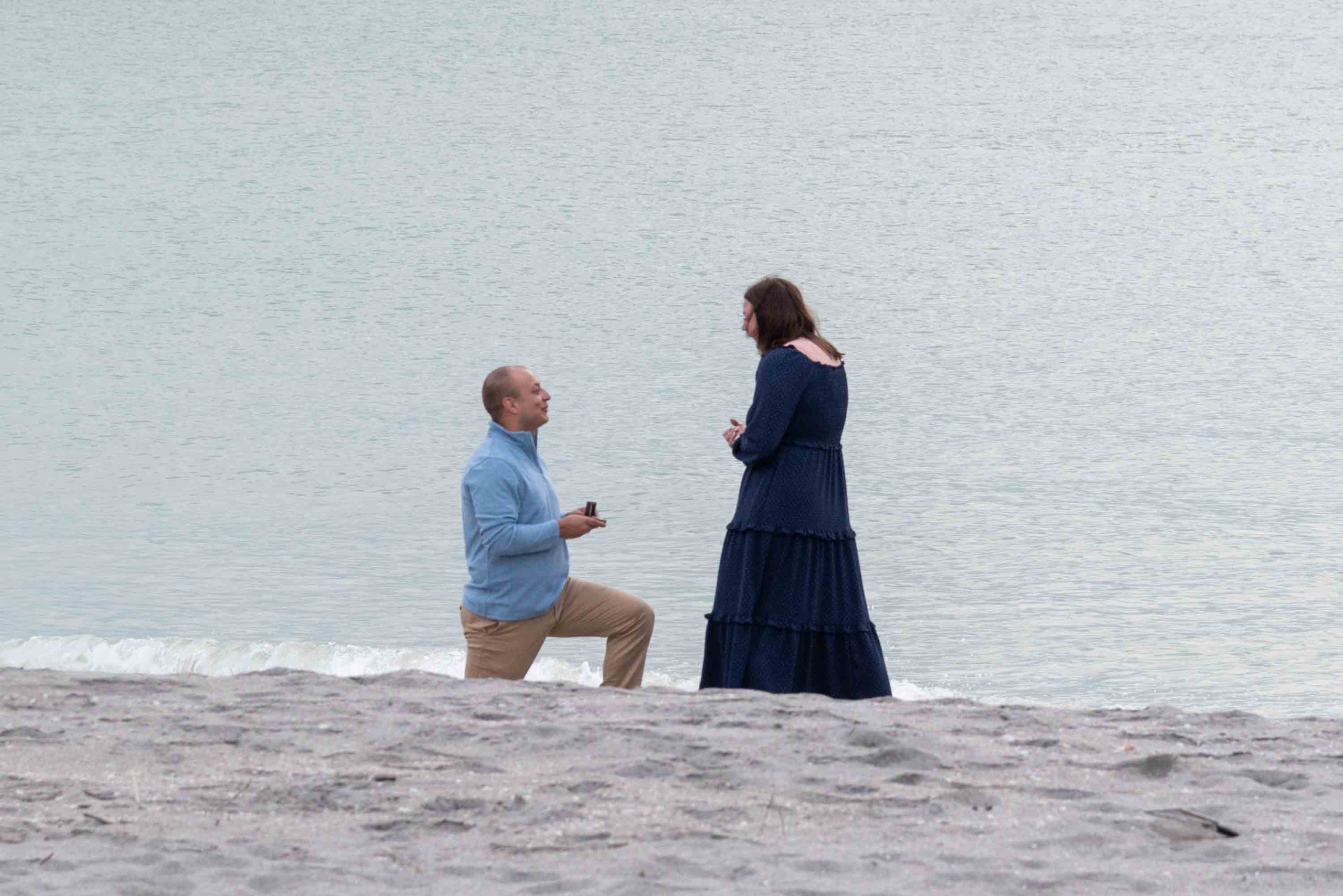 guy gets down on his knee to propose to his girlfriend on the beach