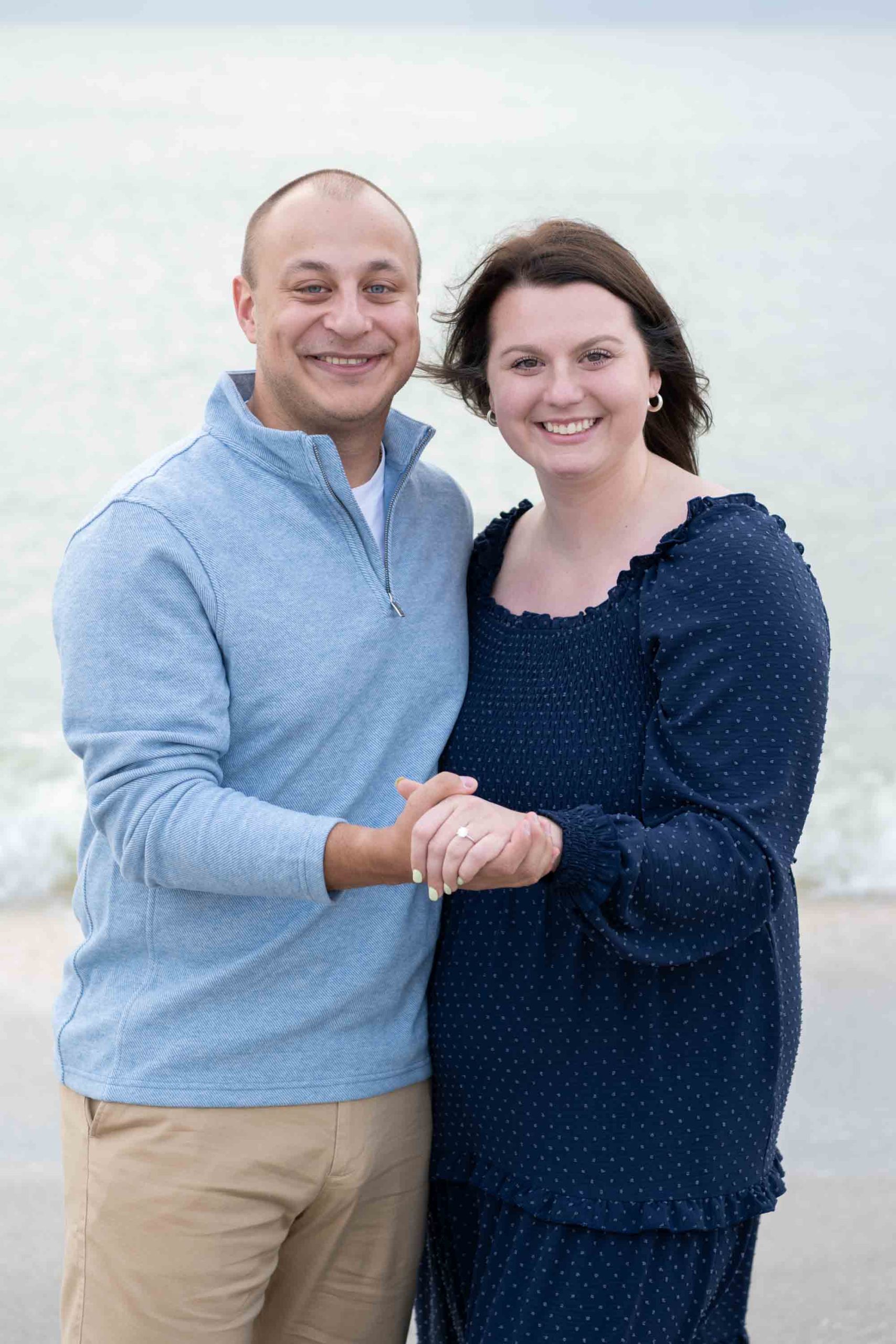 couple hold hands showing off her engagement ring on the beach