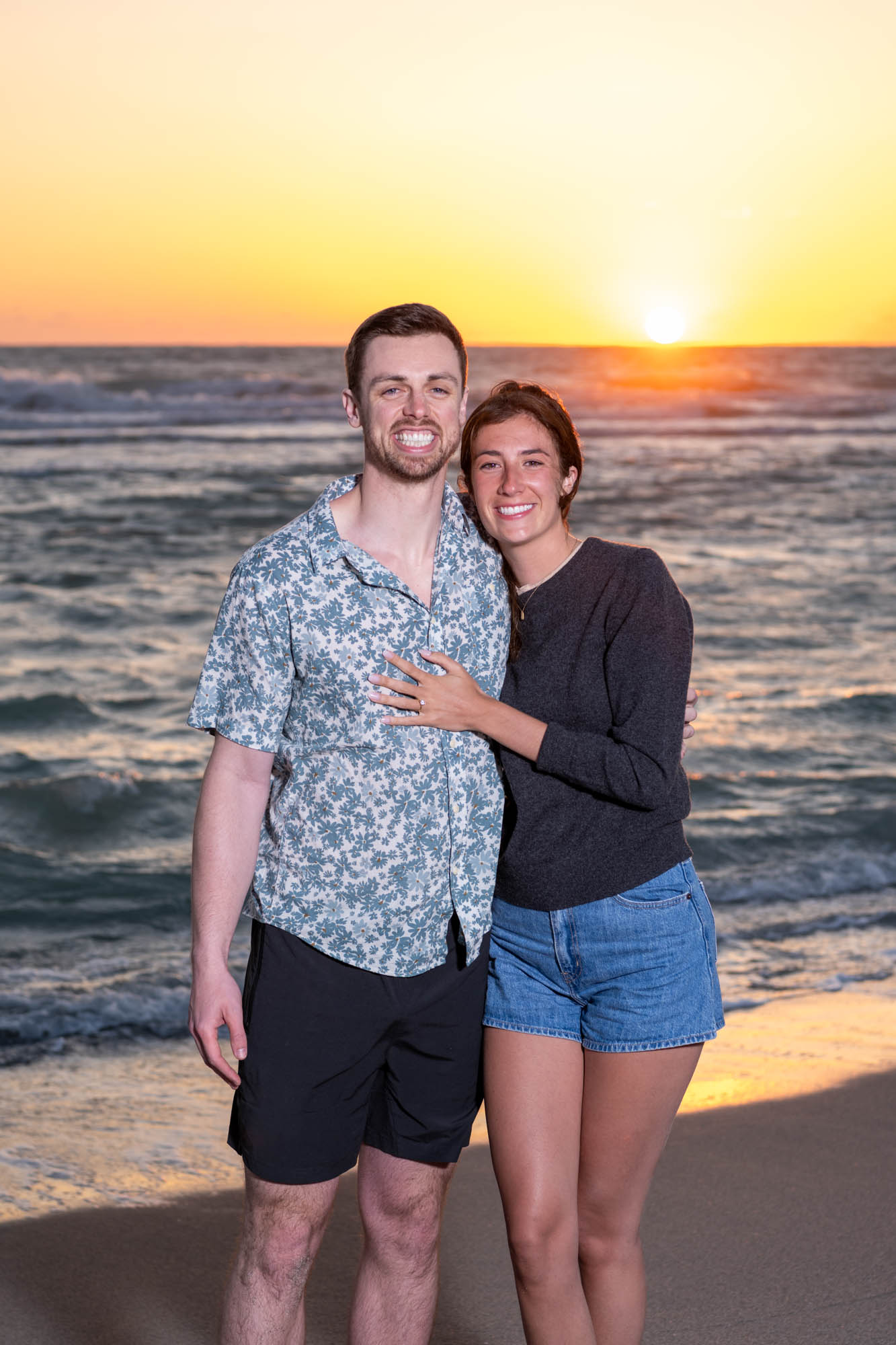 couple smile as the sun sets behind them on the beach