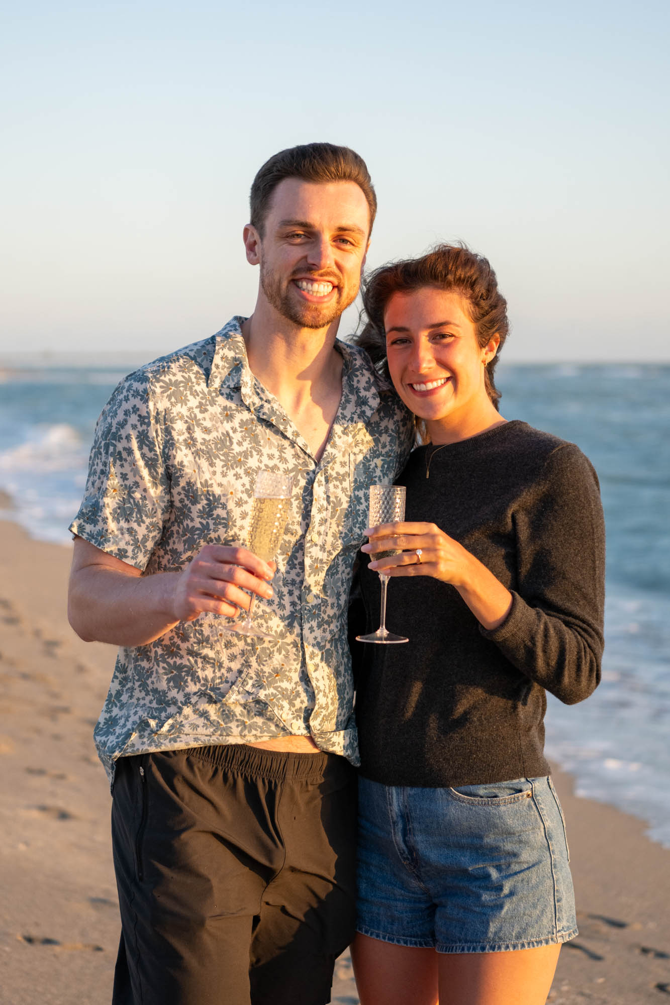 newly engaged couple share a glass of champagne on the beach