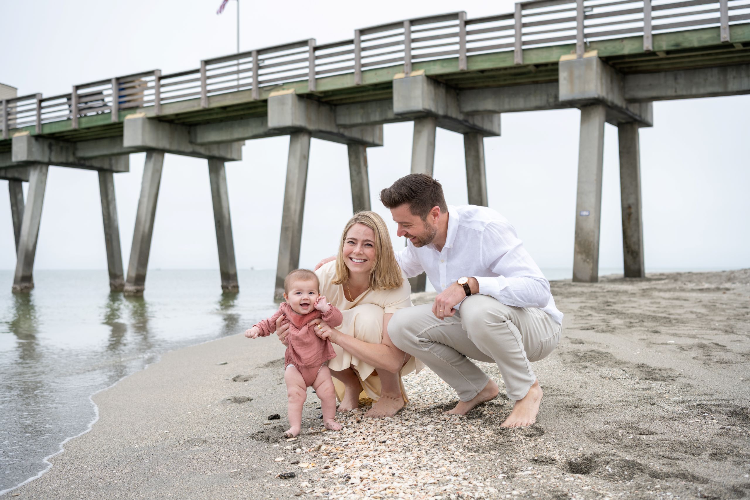 young parents squat in the sand with their little girl on Venice Beach and laugh with her