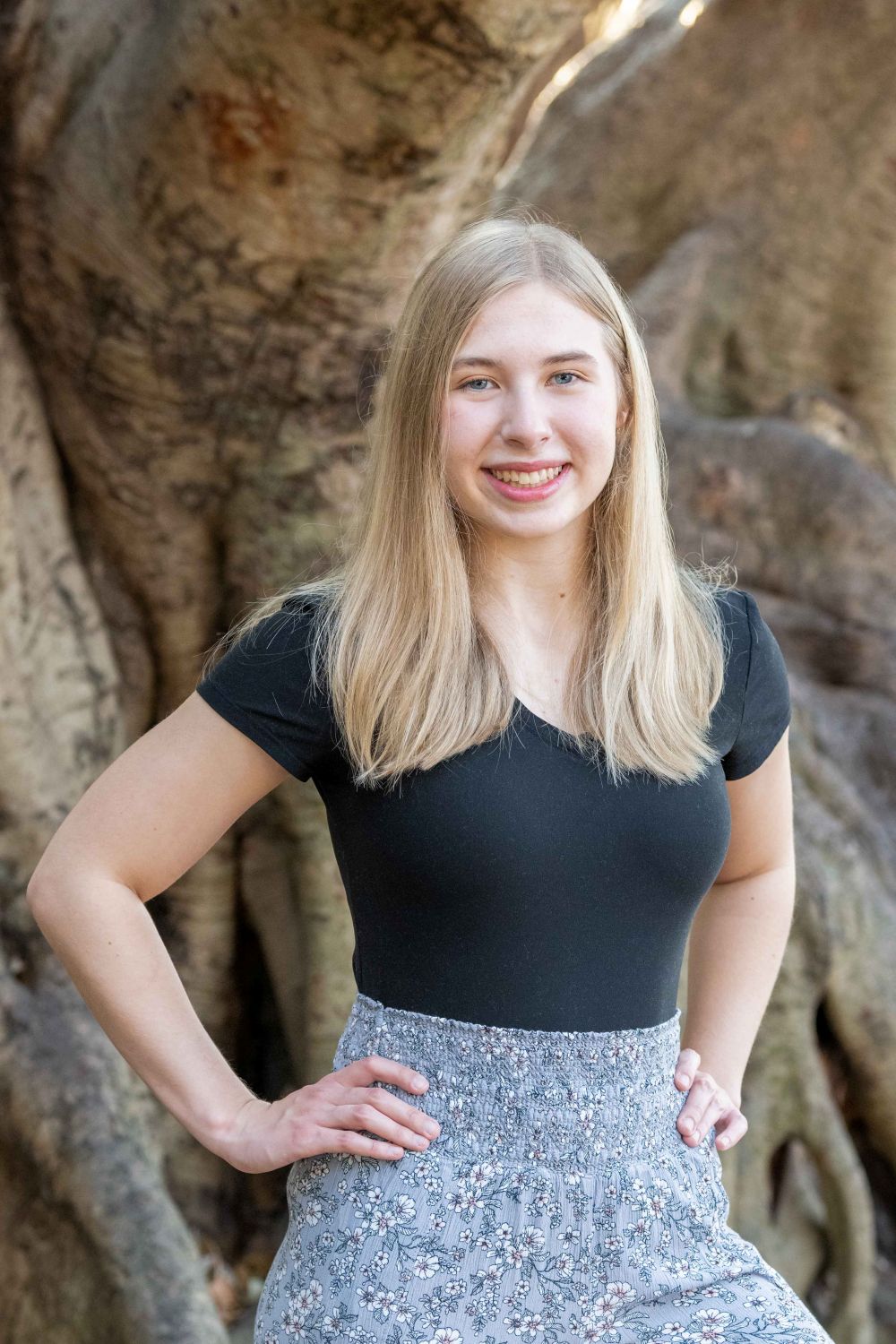 senior photo of girl in black top with her hands on her waist in front of a banyan tree