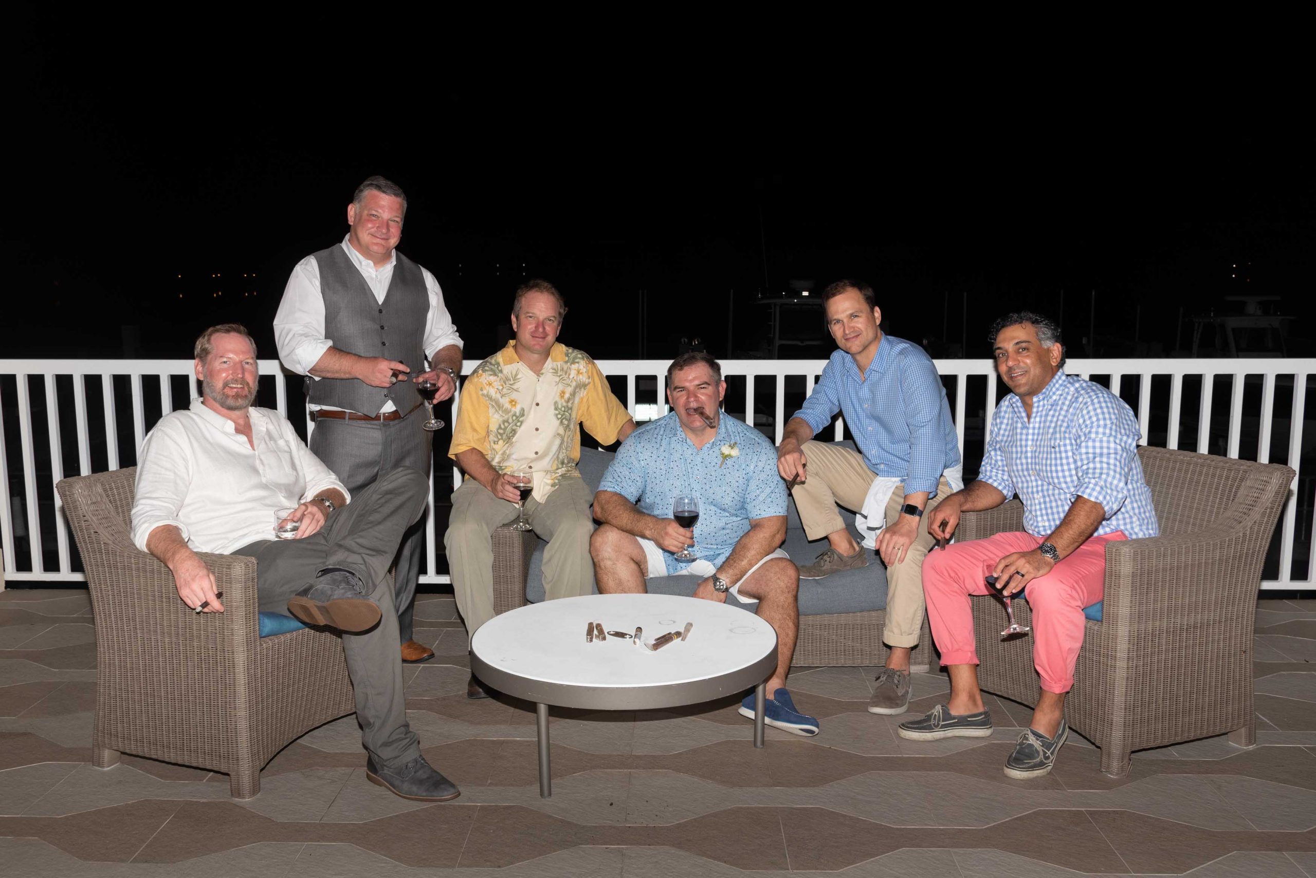 groom and his best friends sit outside on the patio smoking cigars