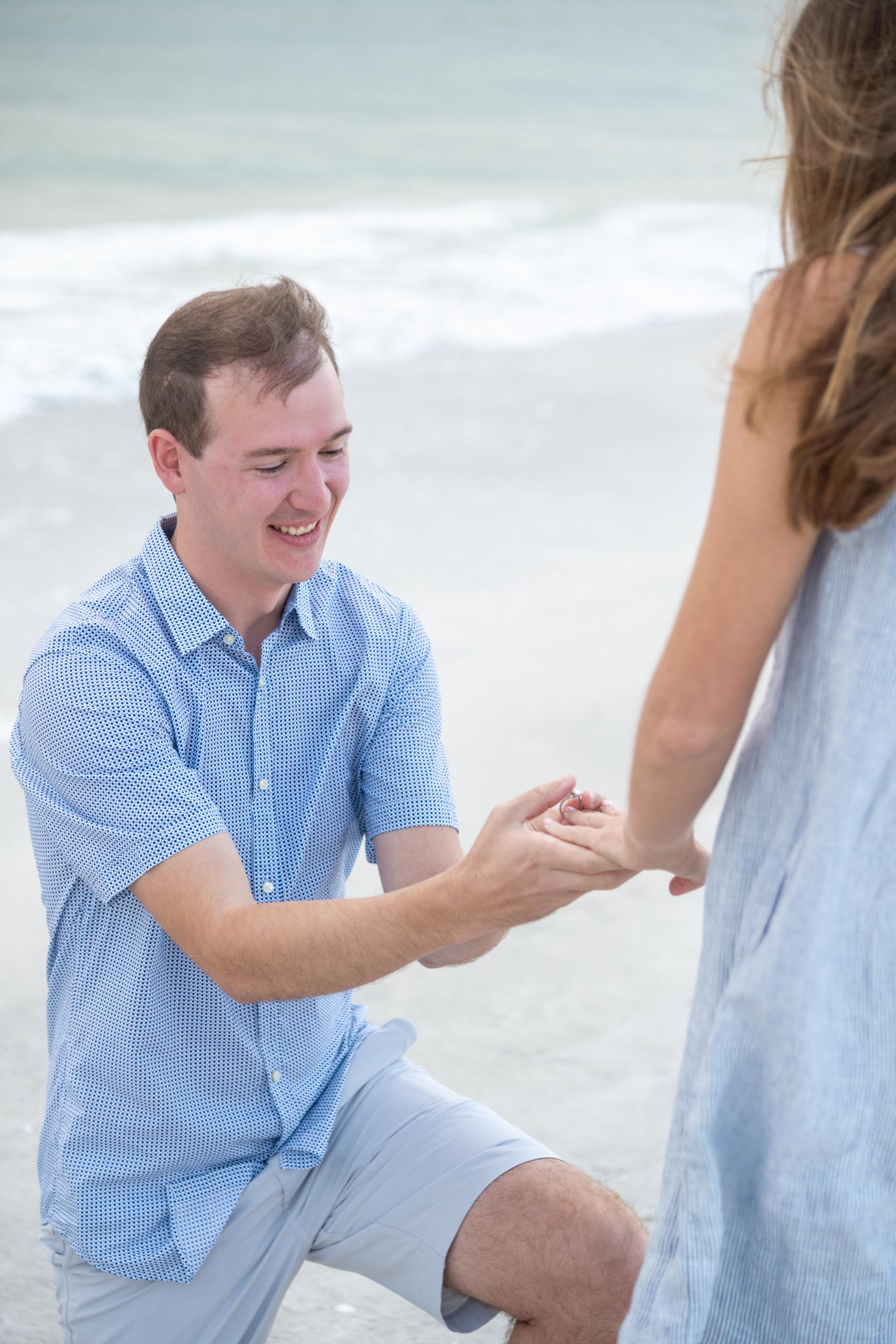 guy on his knee putting a ring on his girlfriend's finger