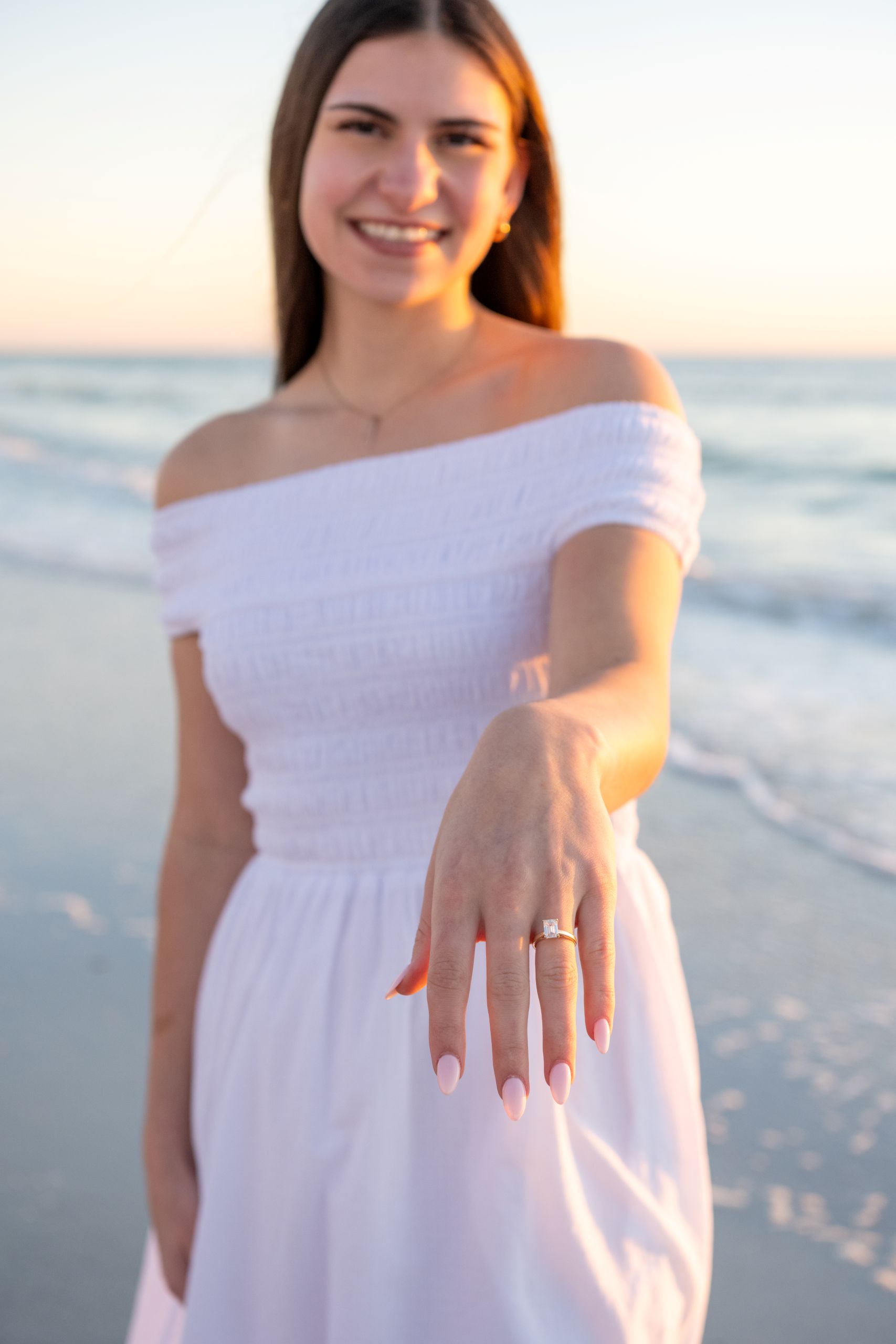 woman in a white dress showing off her engagement ring on the beach