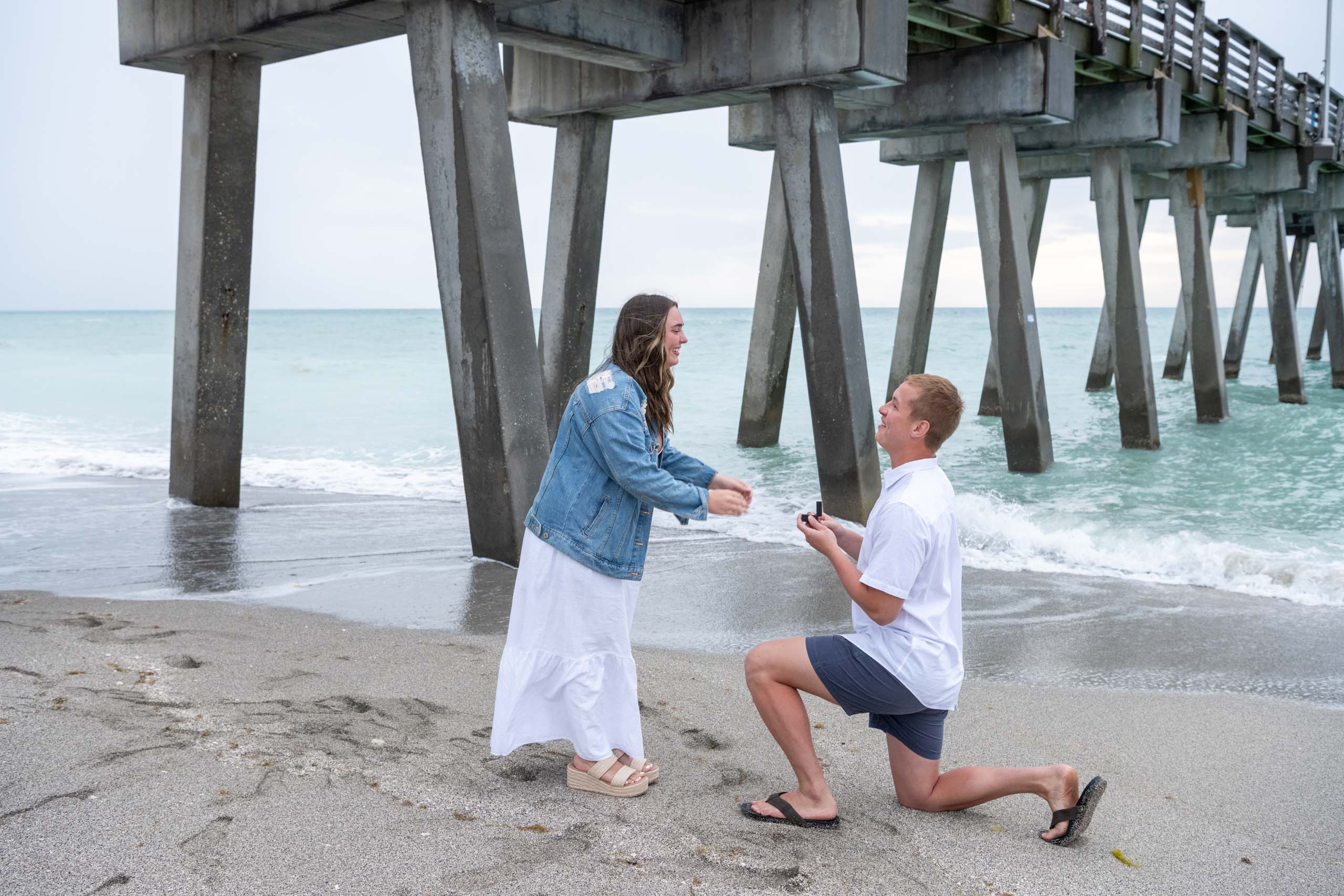 guy down on his knee by Venice Pier to propose to his girlfriend