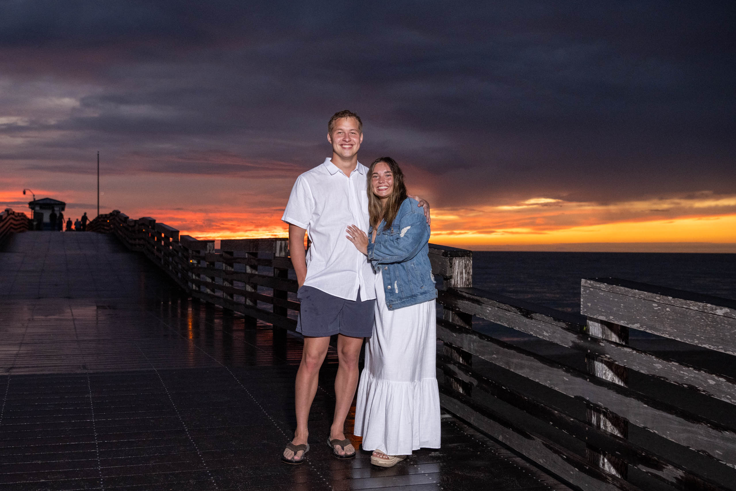 couple stand on the Venice Pier smiling as the sunsets