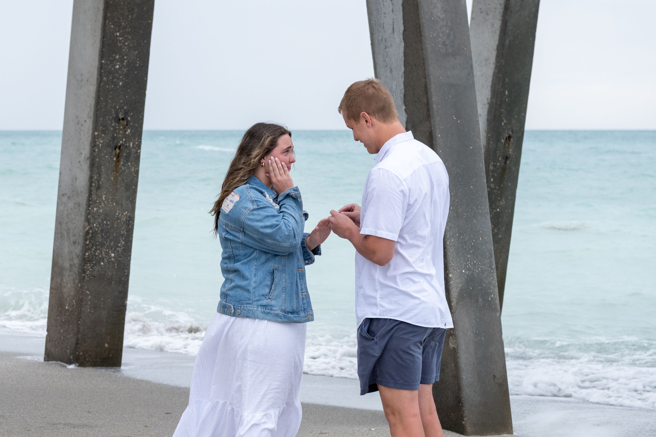 woman holds her hand to her face as her boyfriend puts on an engagement ring