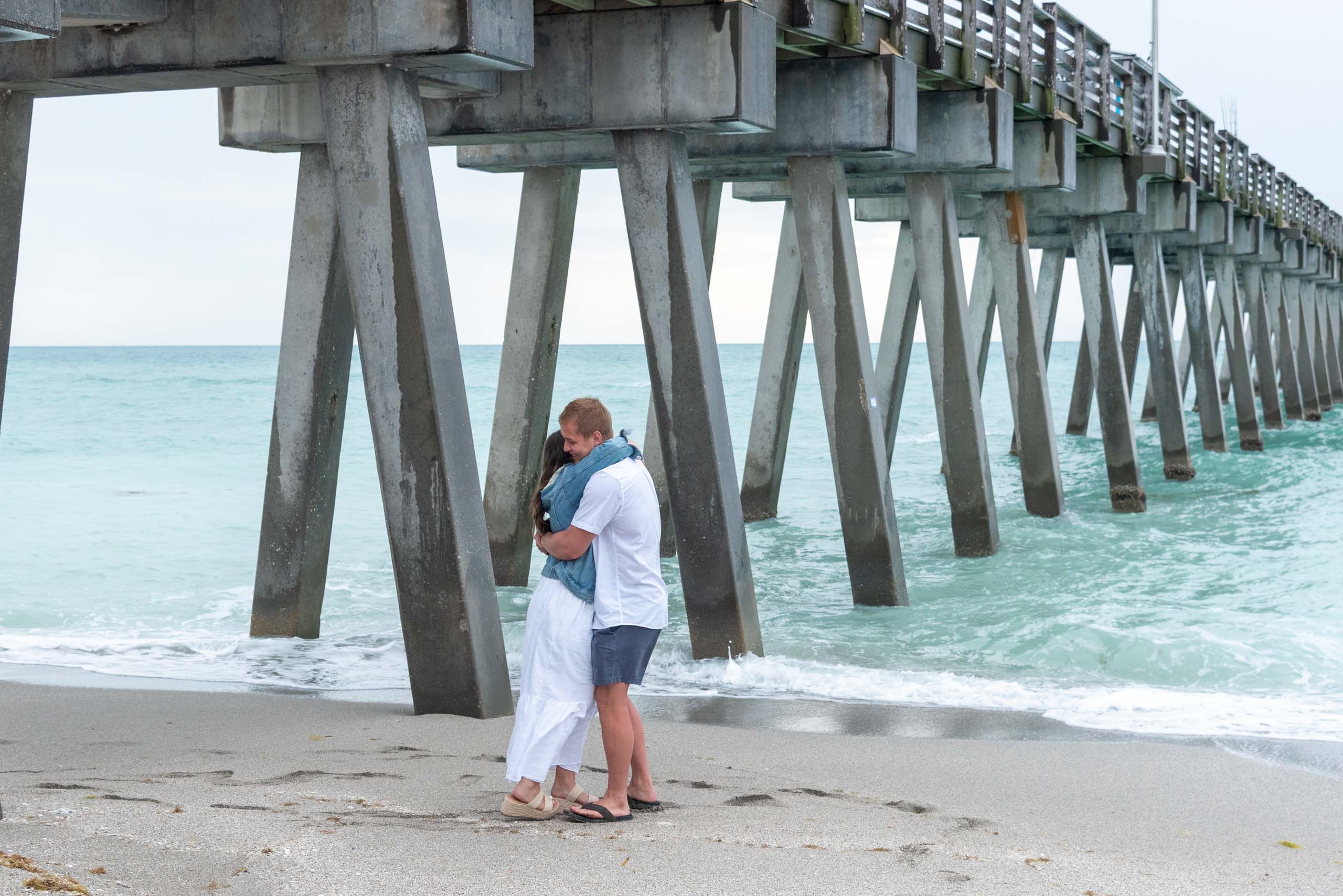 newly engaged couple hug after surprise proposal by Venice Pier