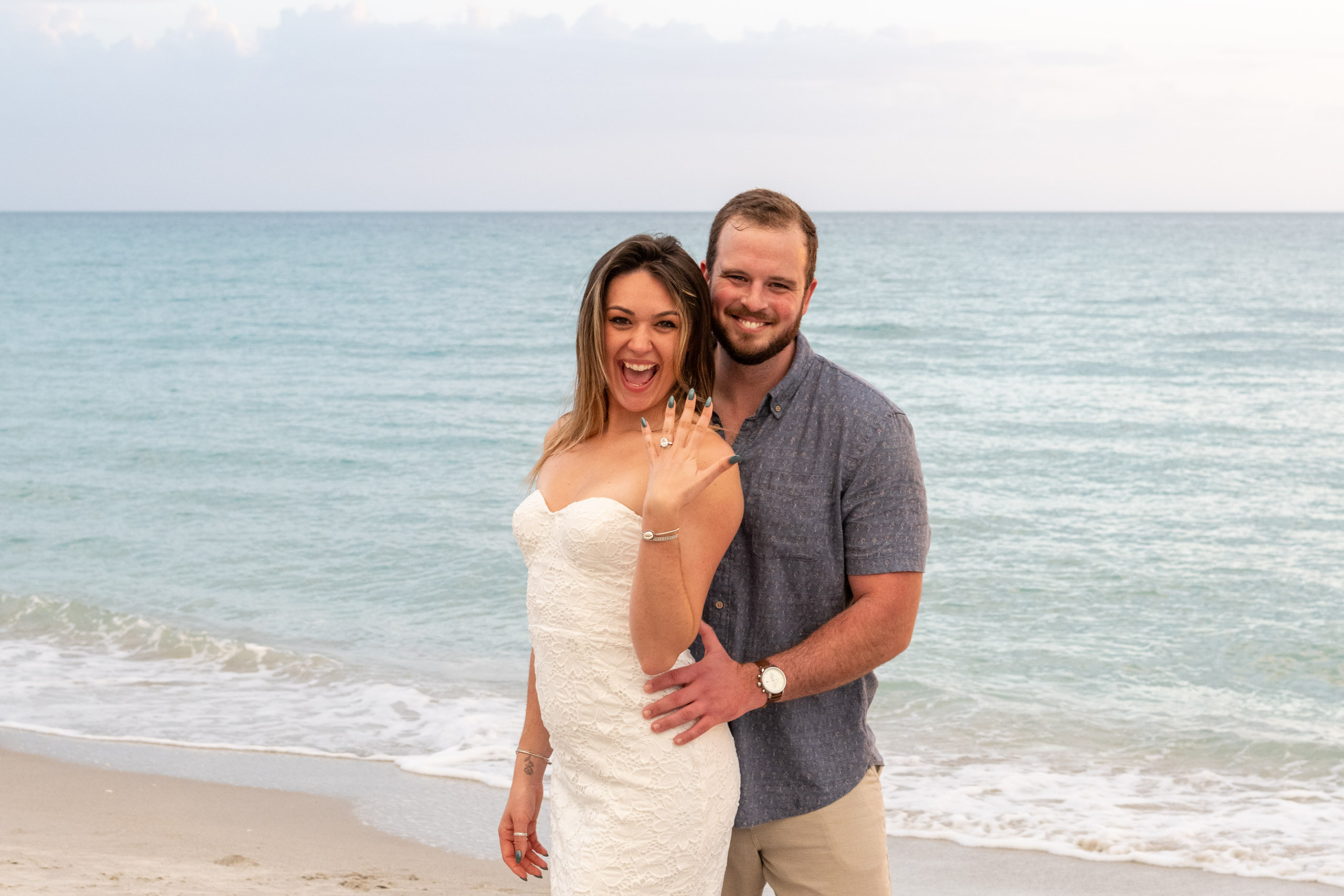 girl shows off her engagement ring after surprise proposal on the beach