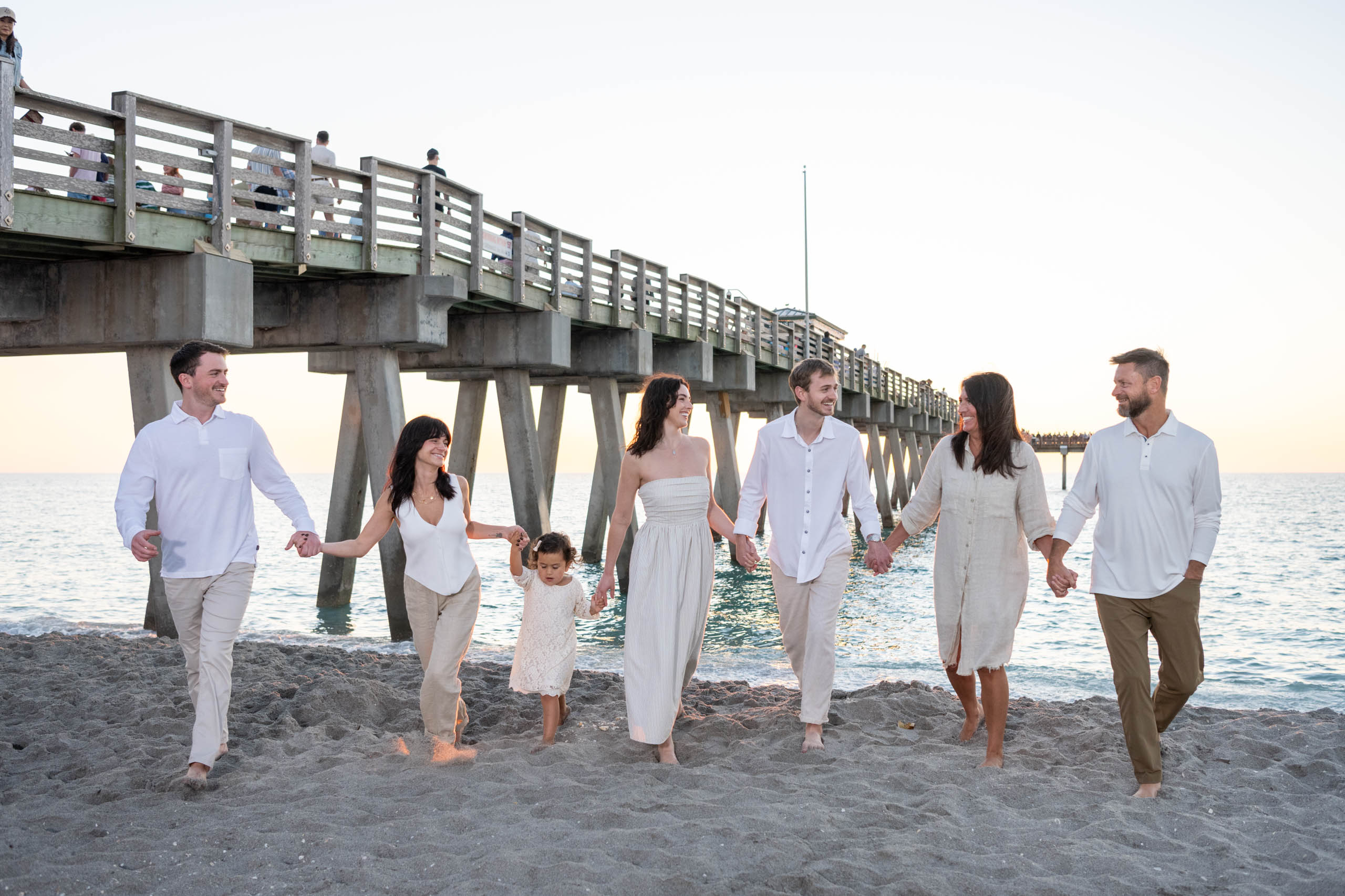 family walks along the beach with the fishing pier in the background