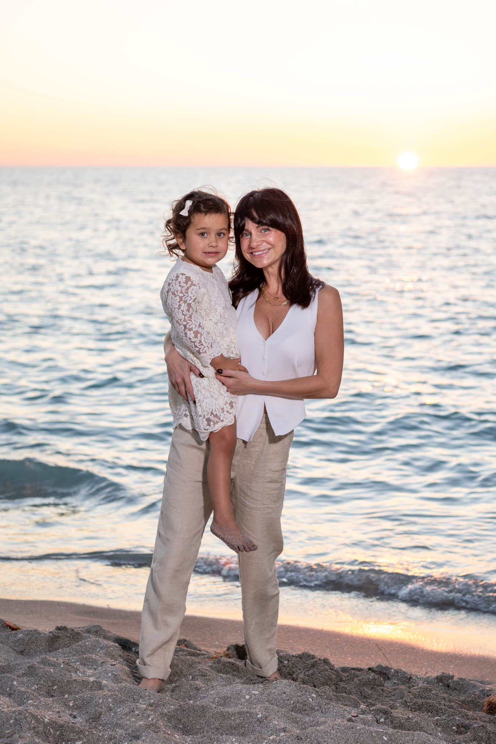mom holding her young daughter on her hip on the beach at sunset