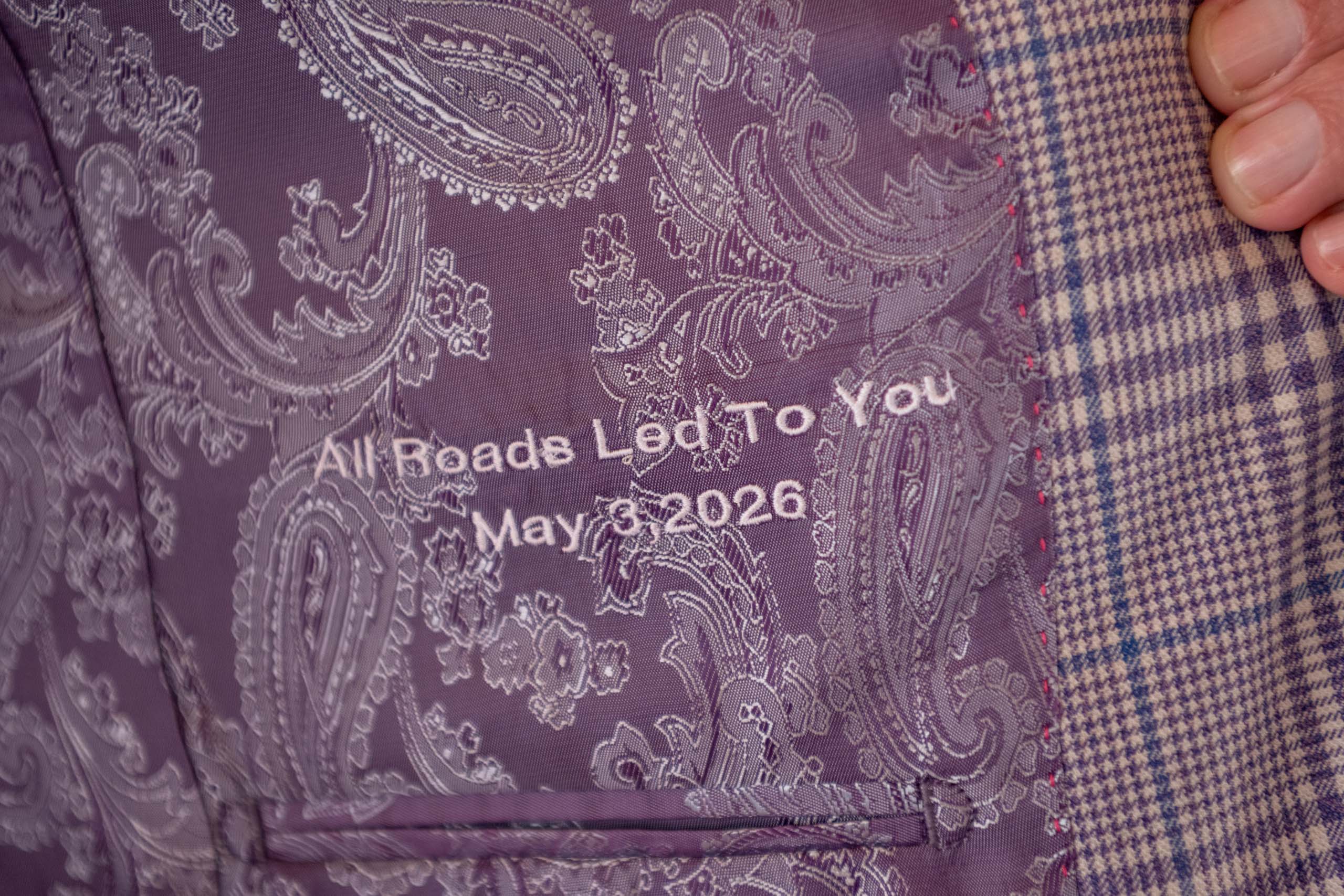 custom embroidery inside grooms suit that says "all roads let to you May 2, 2026"