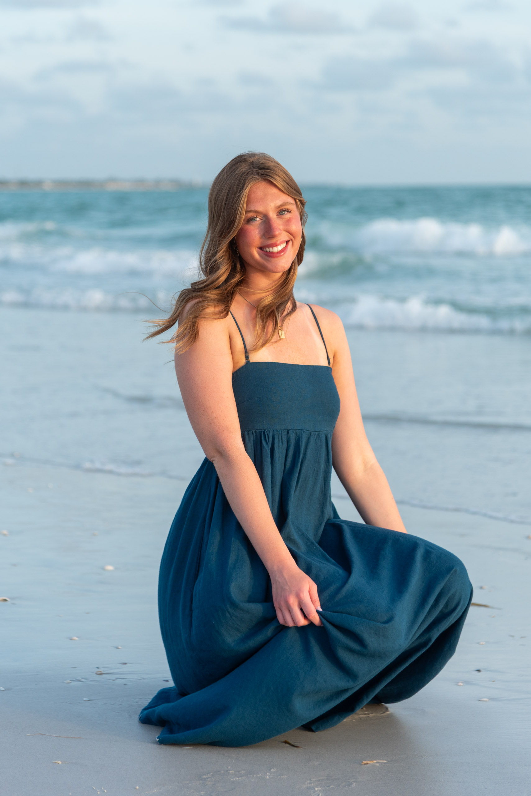 senior girl in teal dress sitting on the sand on the beach