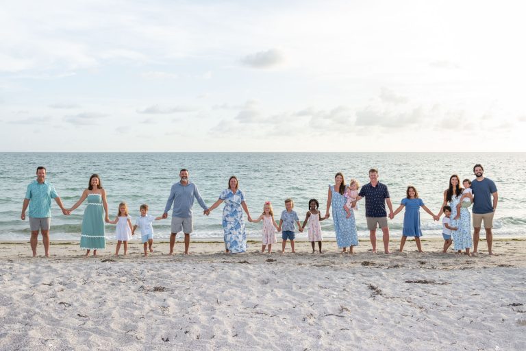 large family holds hands while standing on beach with Gulf behind them