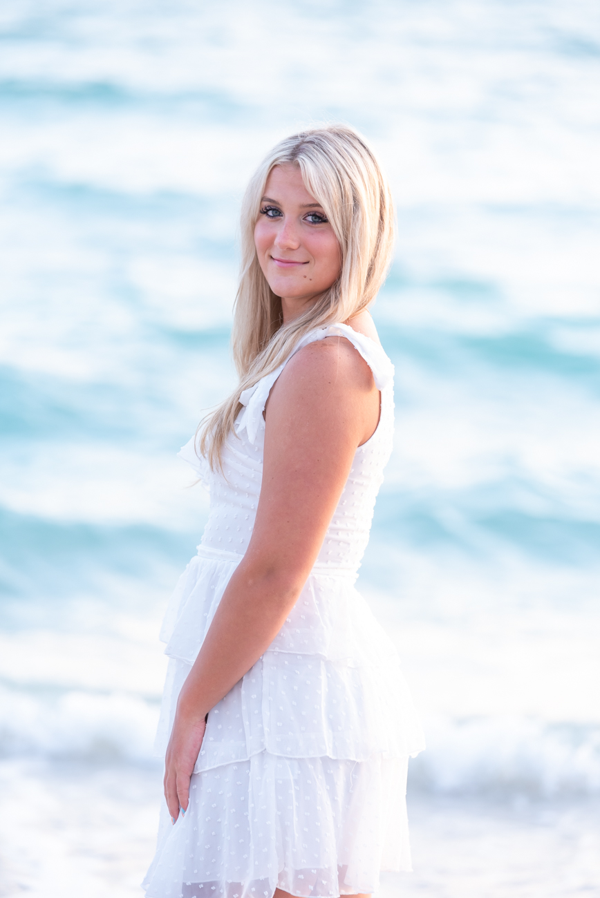 blonde girl in white dress on beach with water in the background
