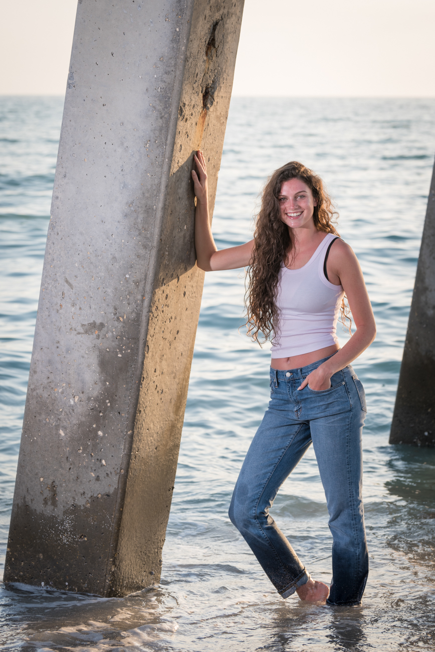girl leaning up against pier post with a white crop top and blue jeans