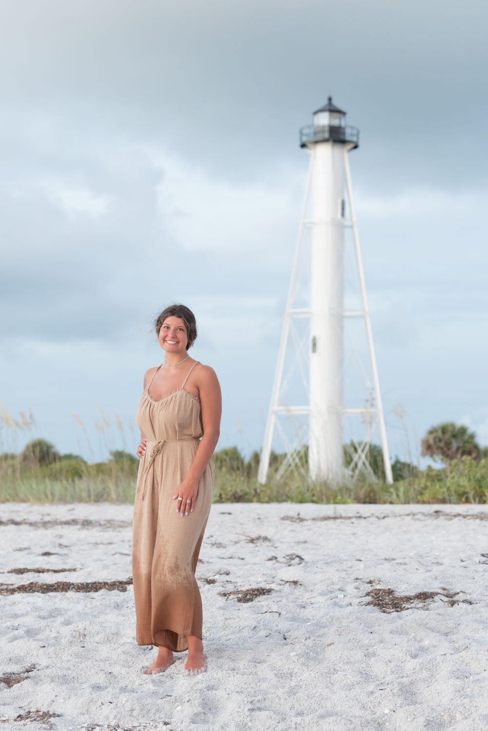 senior photo of girl in brown jumpsuit on the beach in front of a lighthouse