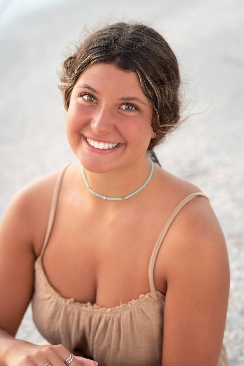 senior girl with a choker necklace and brown top sitting on the beach