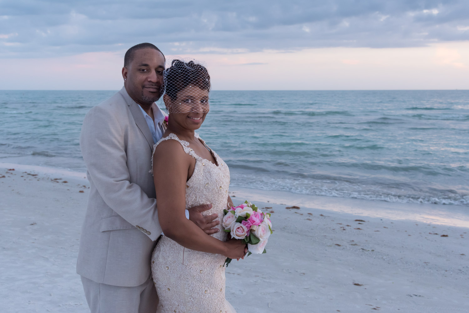 groom holds bride from behind as they stand on Siesta Key Beach after their wedding