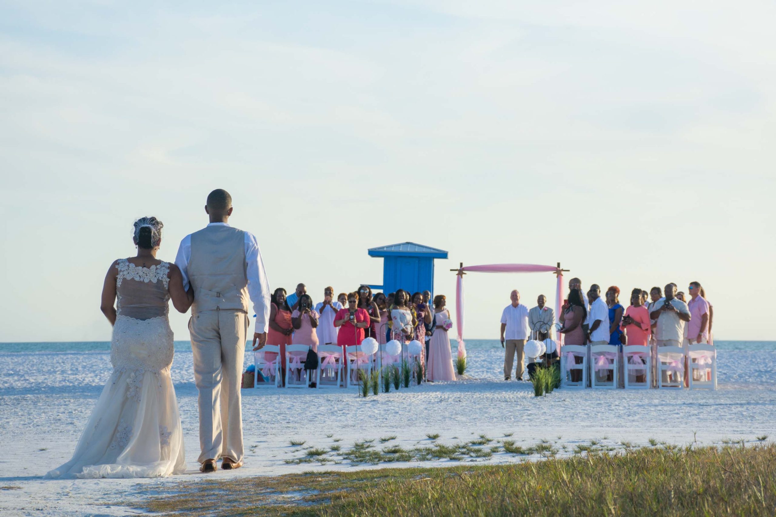 bride being escorted by her son as the wedding party turns to see her approaching the arch and her husband on Siesta Key Beach