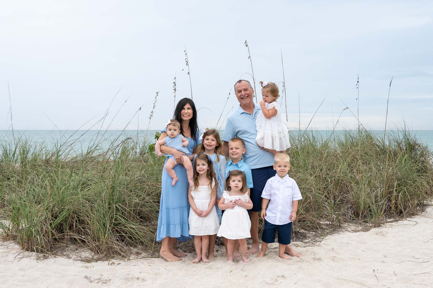 grandparents with their seven grandchildren on Casey Key Beach with seagrass and the Gulf behind them
