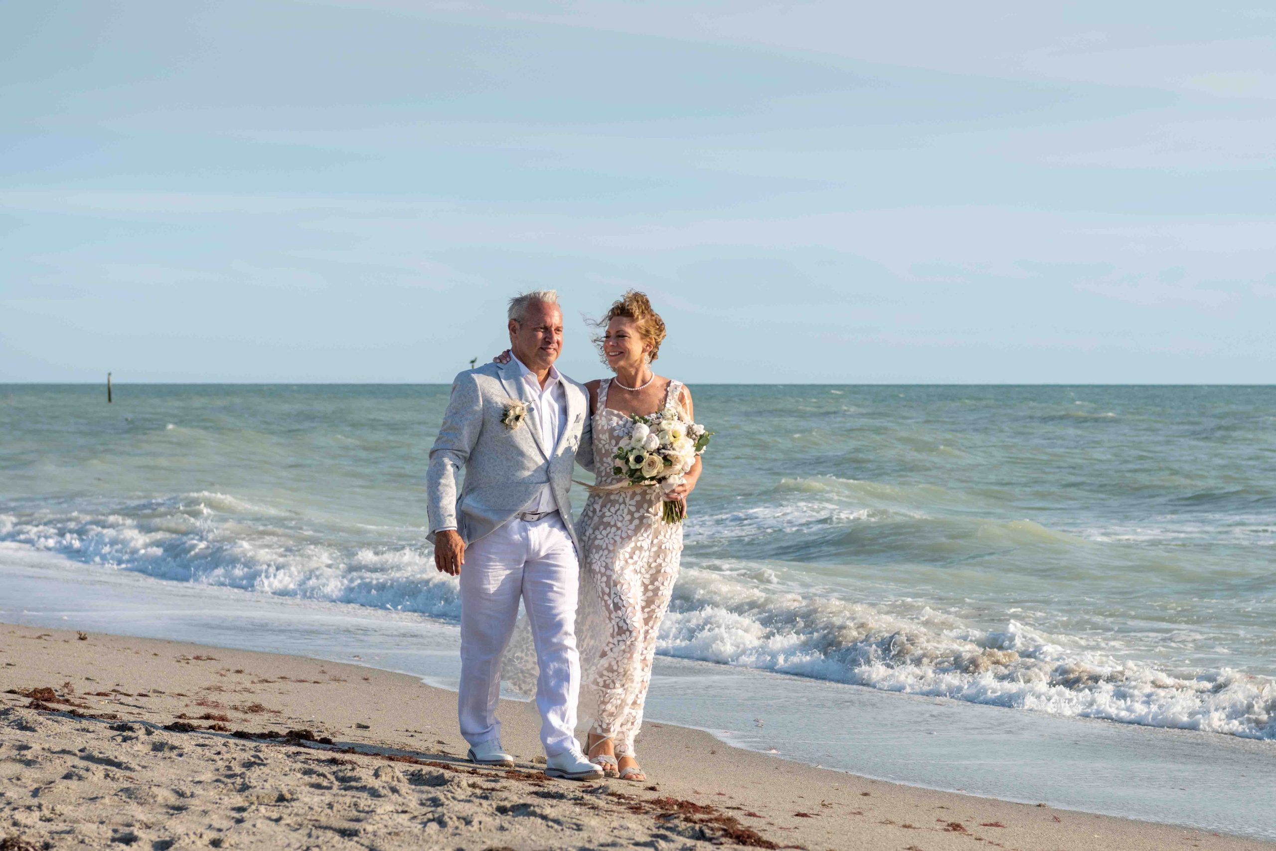 married couple walk hand in hand along the beach