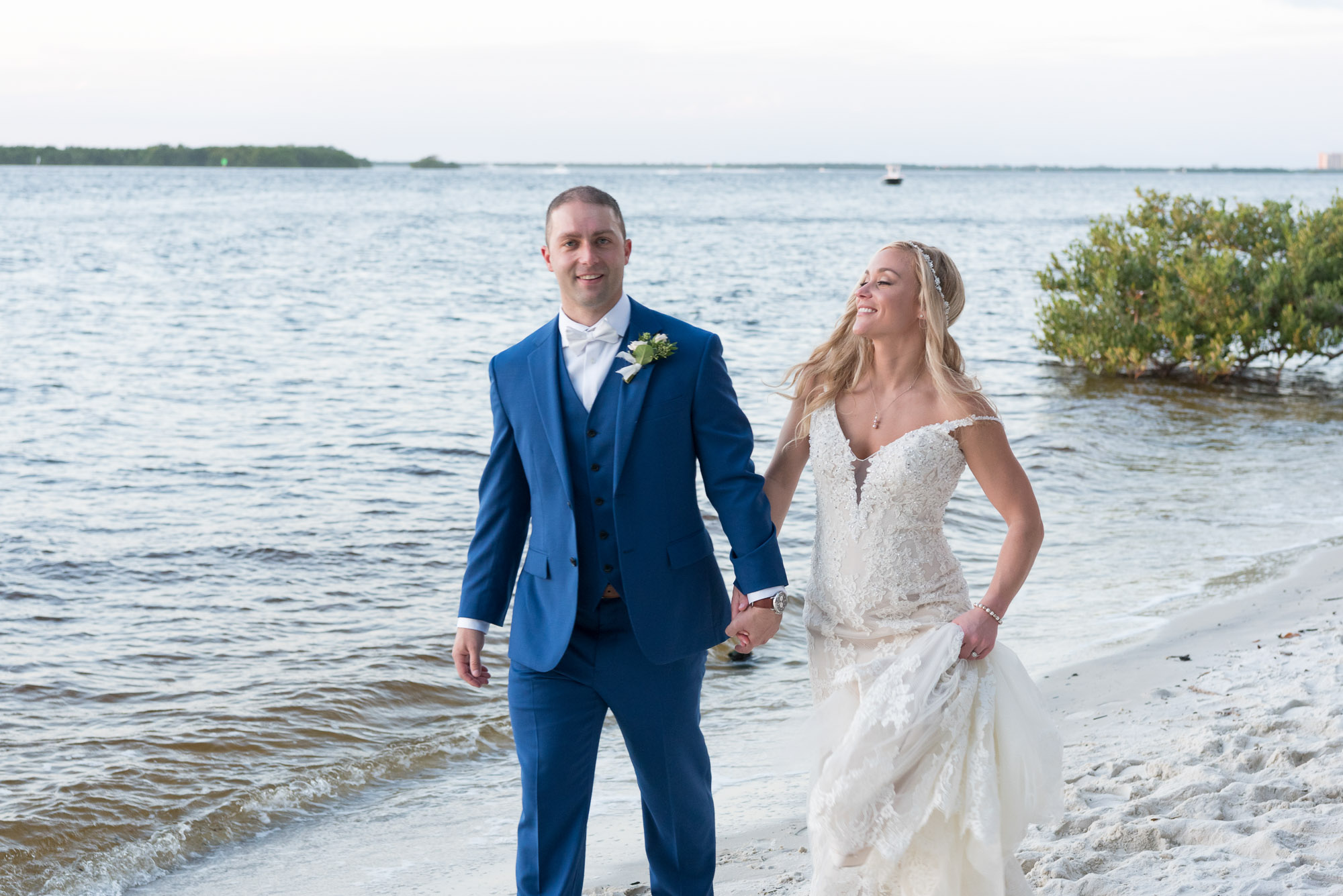 bride and groom walk along the beach after wedding