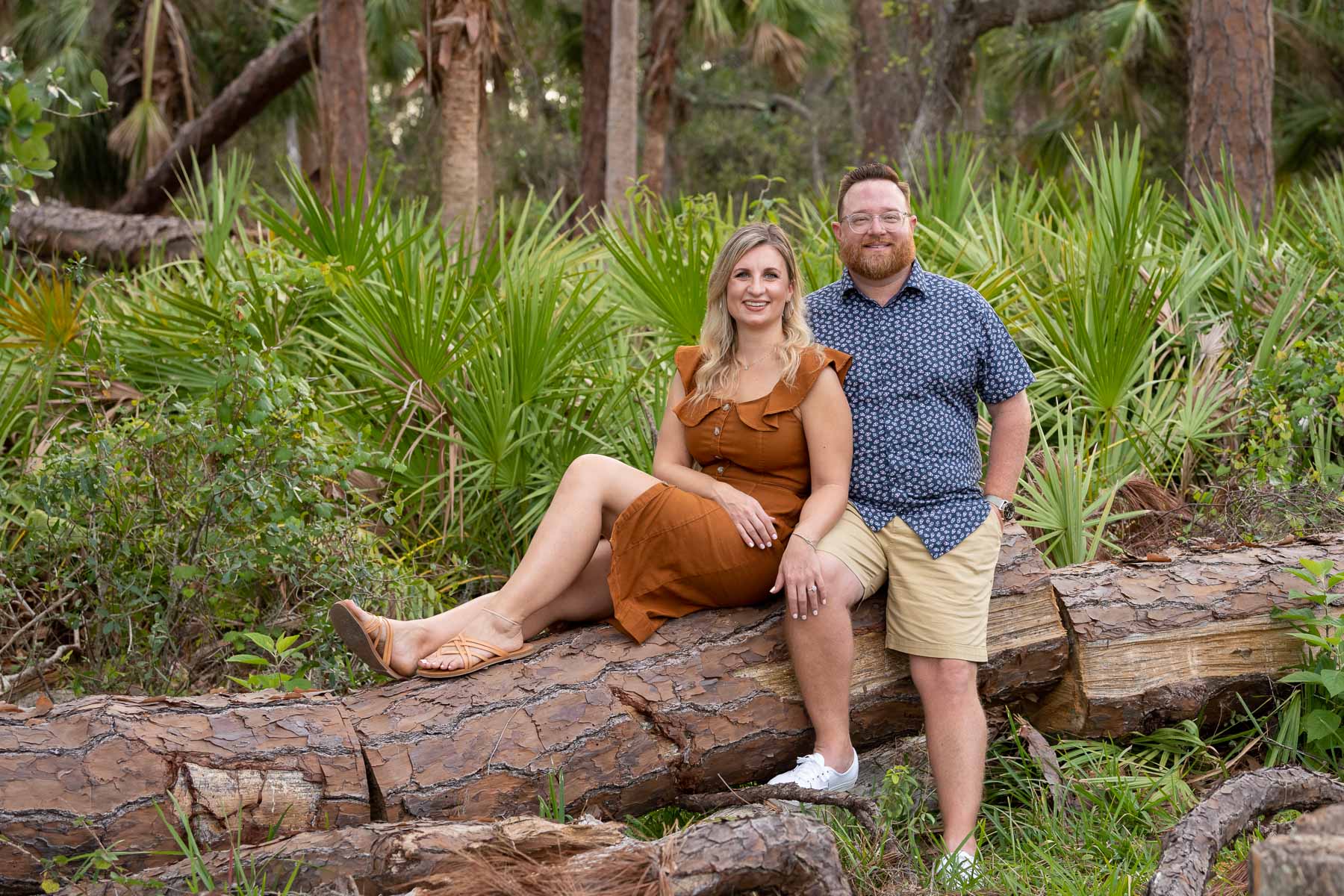 engaged couple sit on a downed tree in a park