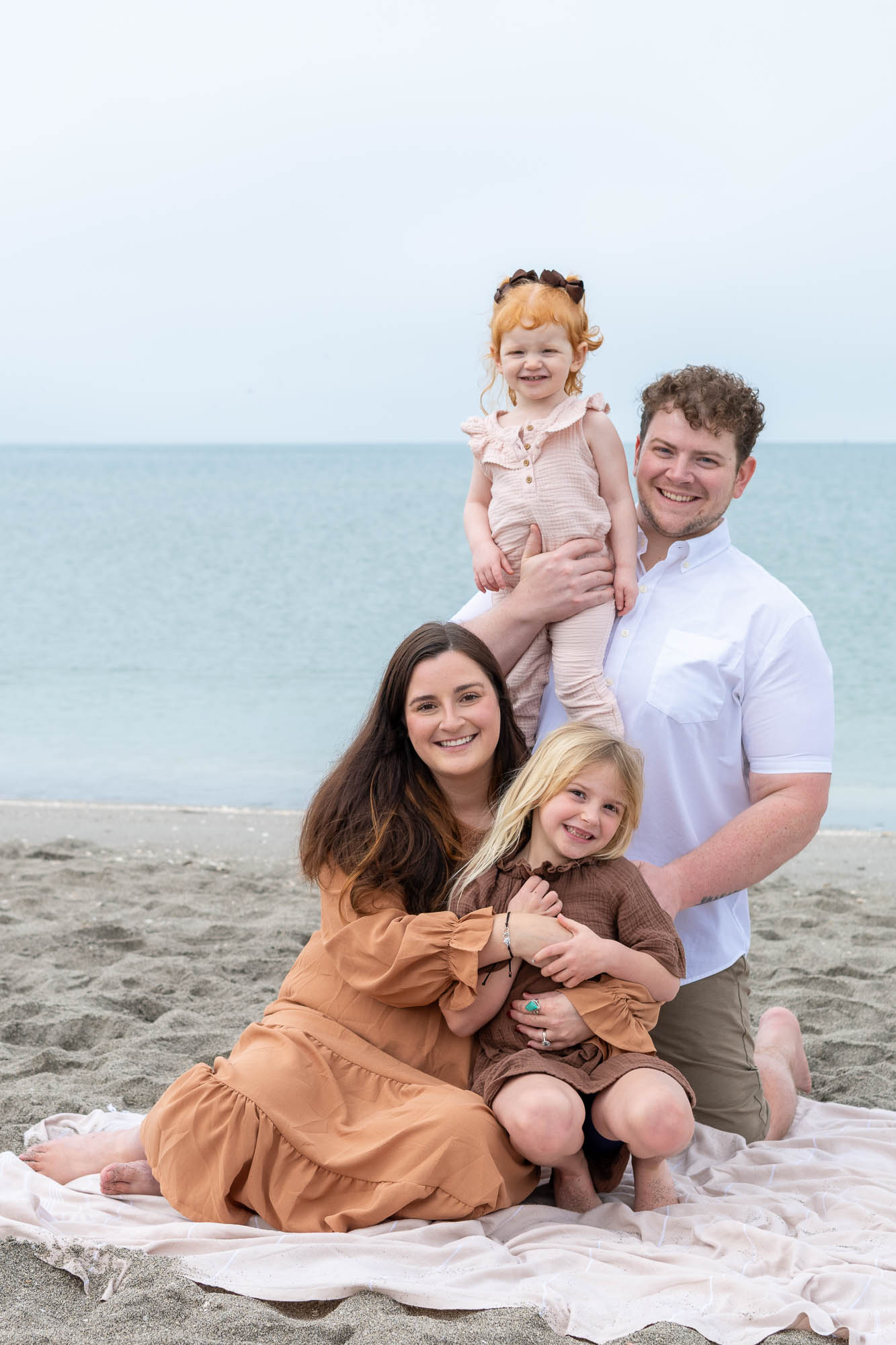 parents play with their two young daughters while sitting on beach blanket