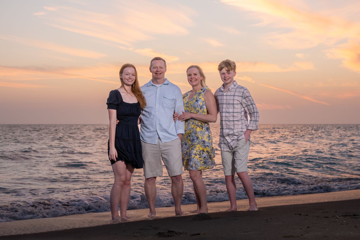 family of four stand together on Manasota Key with a beautiful sunset behind them