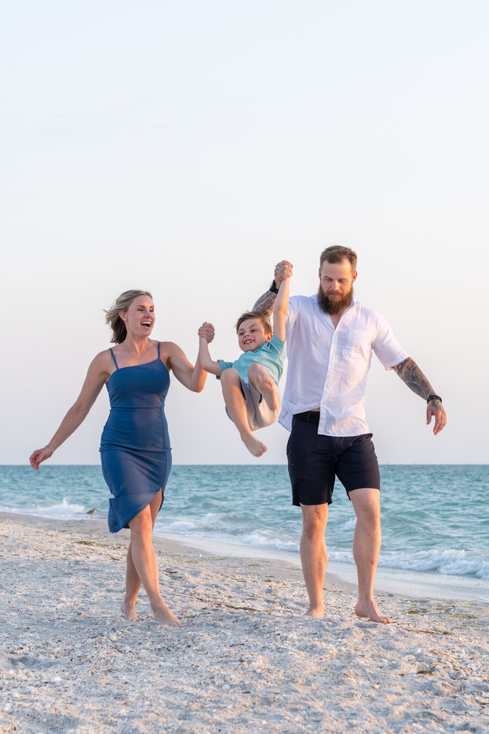 couple swing their son as they walk along the beach