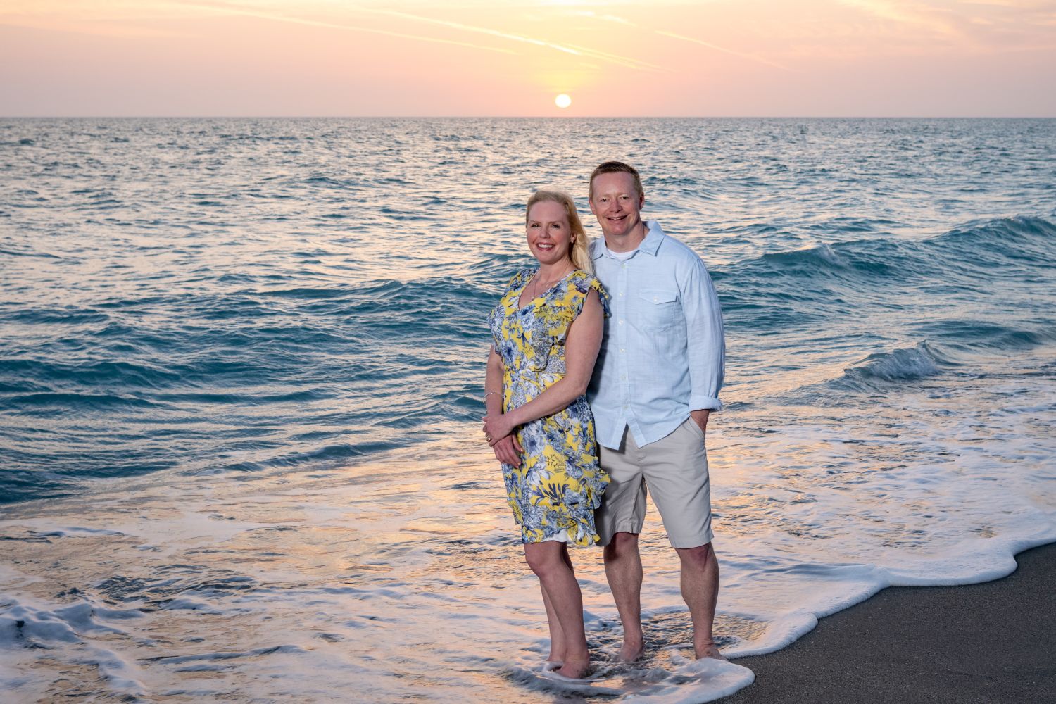 parents standing with their feet in the water at sunset