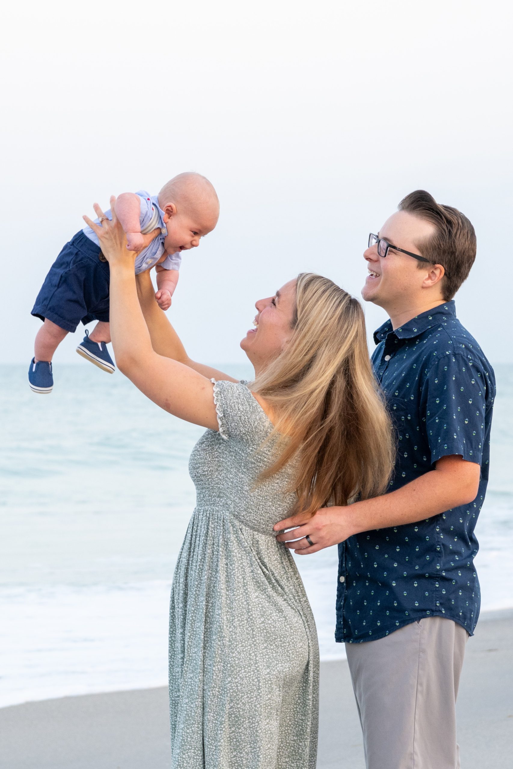 parents raise their son in the air while standing on the beach