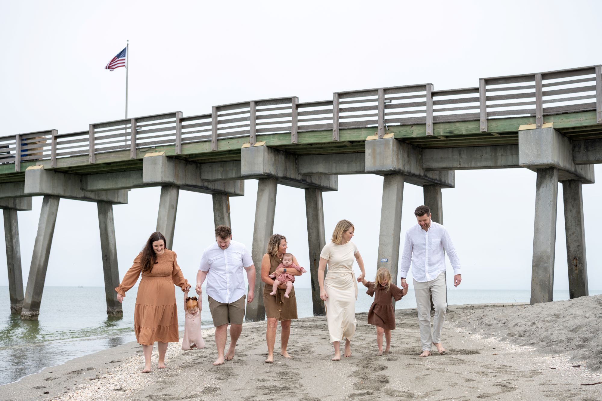 large family walk along the beach with the pier in the background