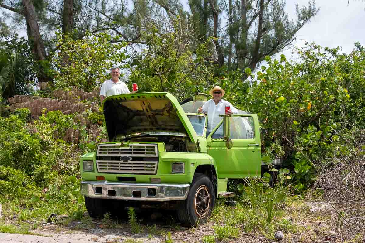 groom and his friend stand on a junky but fun old green truck