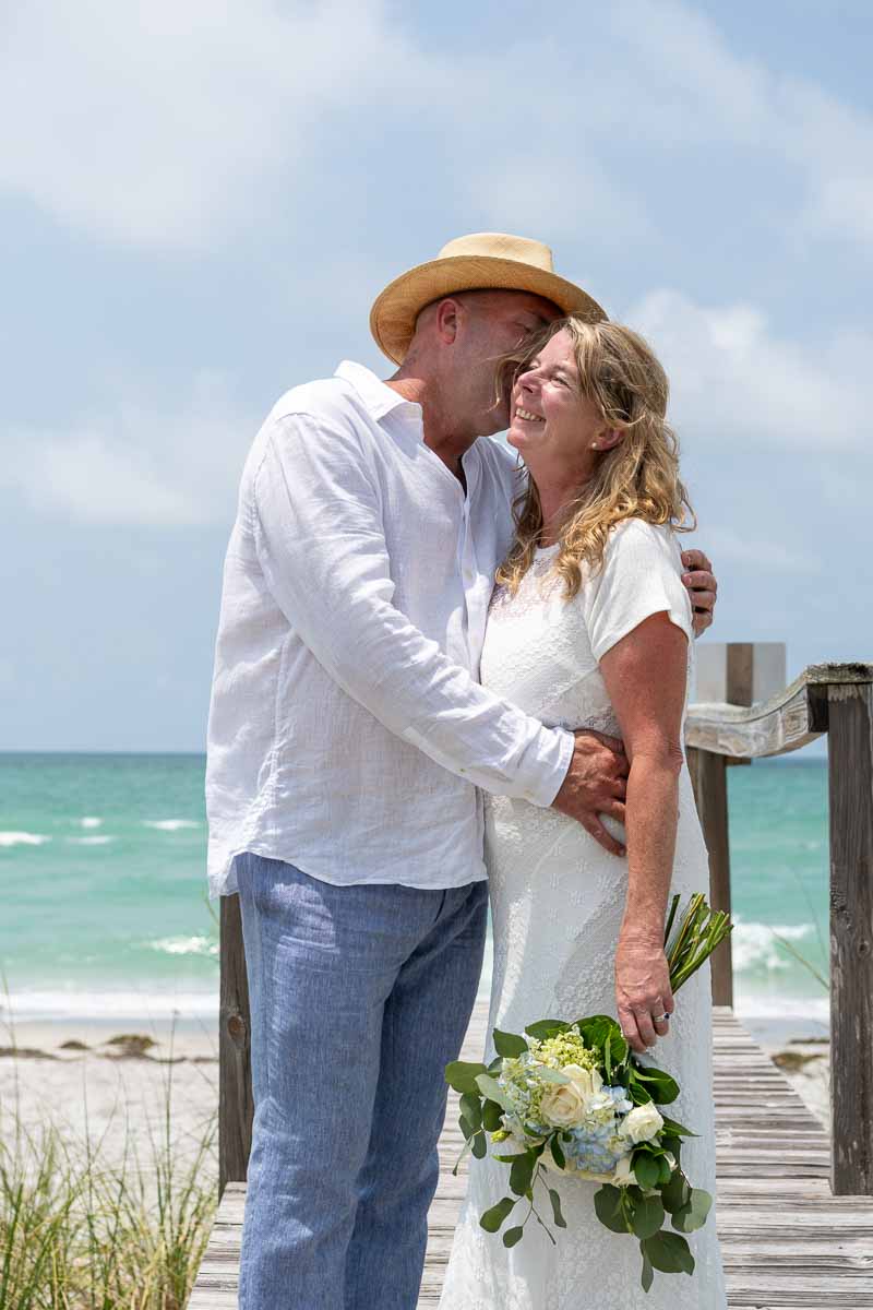 groom whispers in his bride's ear, making her laugh as they stand on a boardwalk with the Gulf behind them.