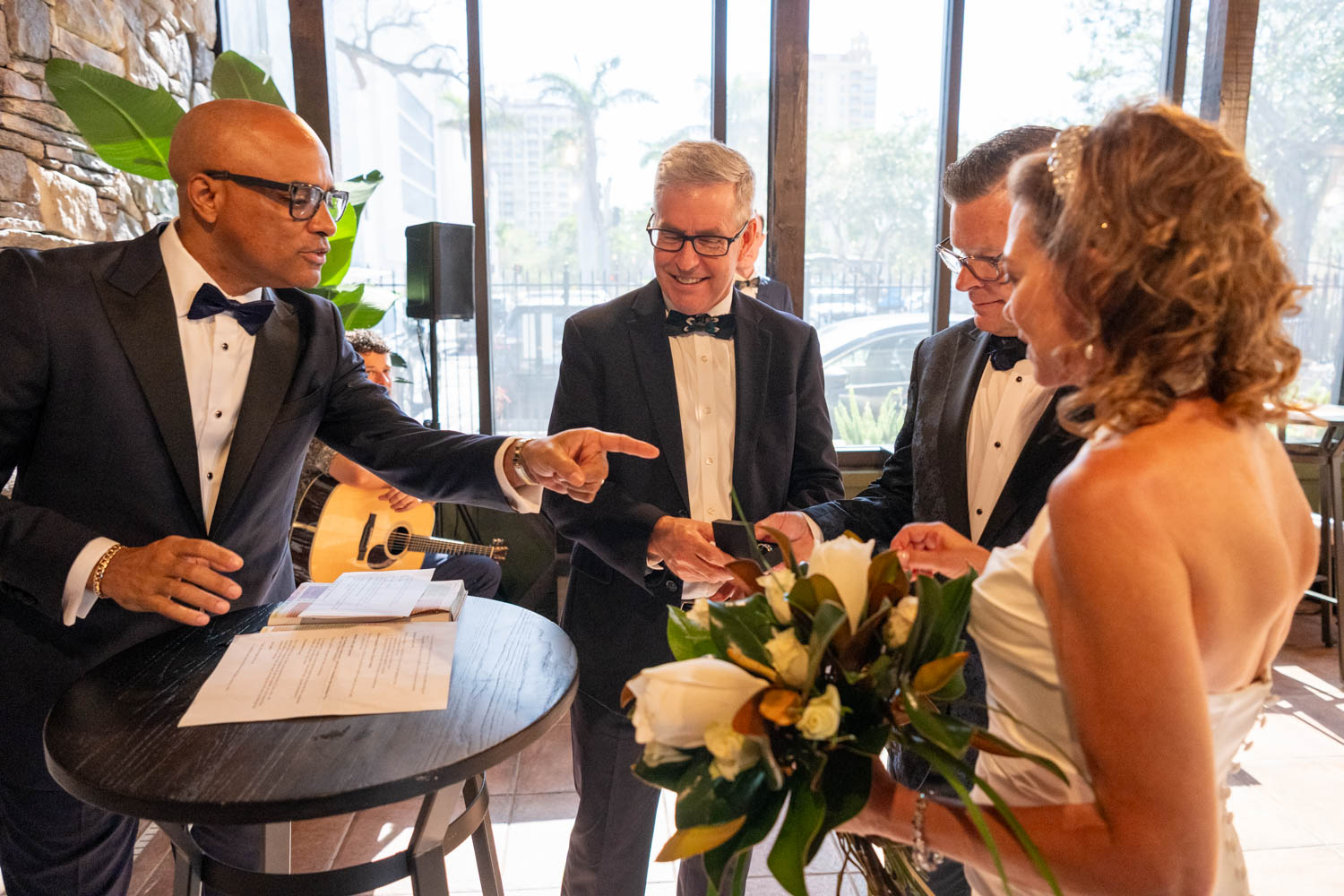 officiant points at wedding rings that the bride and groom are holding