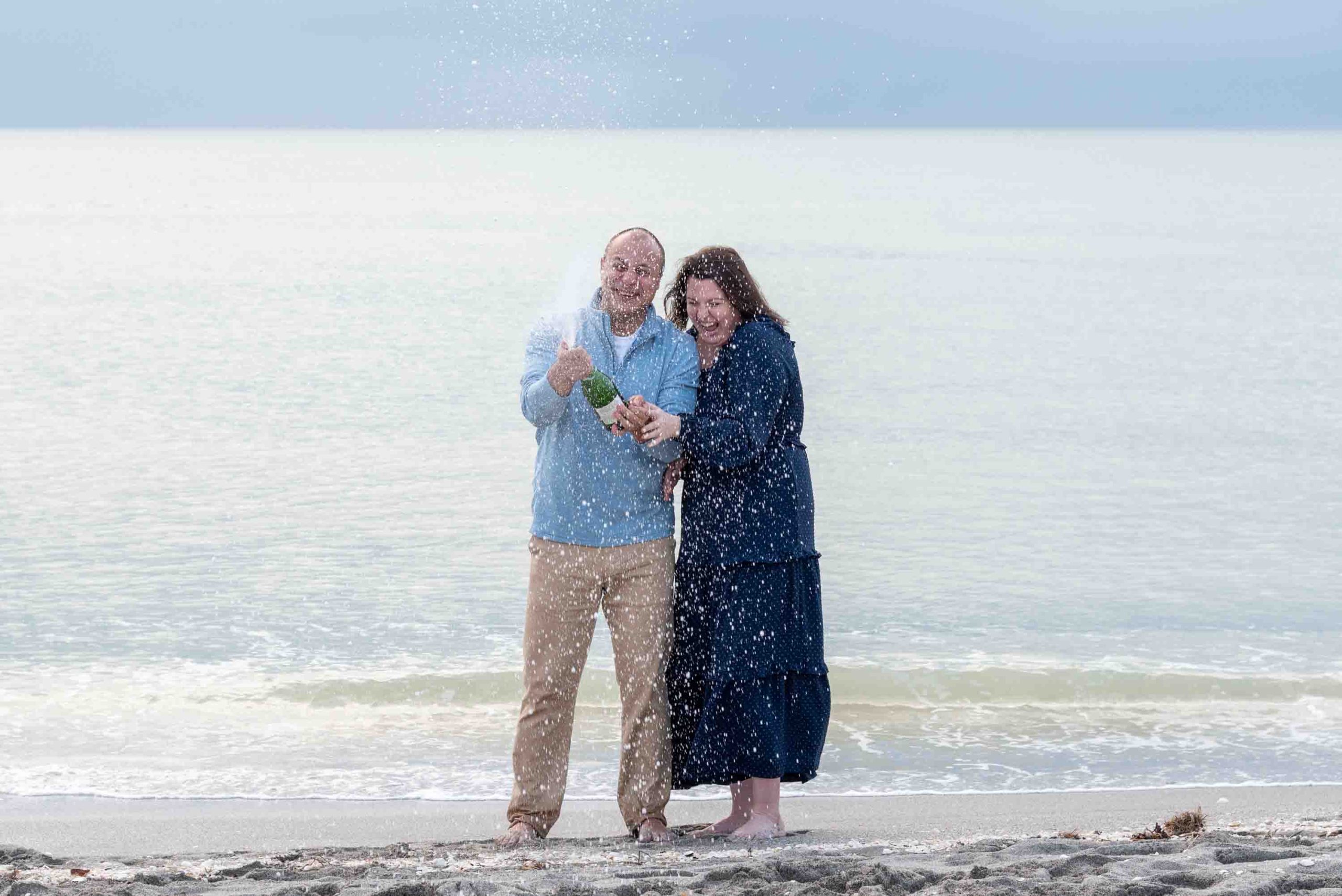couple spray a bottle of champagne on the beach
