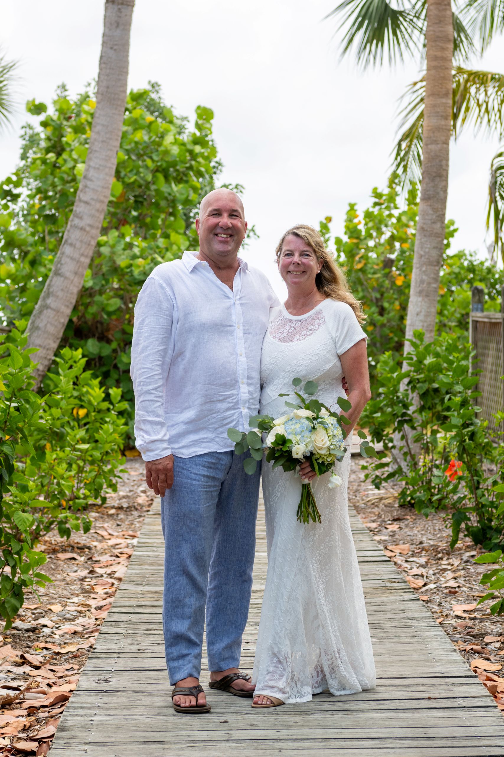 bride and groom stand on a path surrounded by trees and foliage