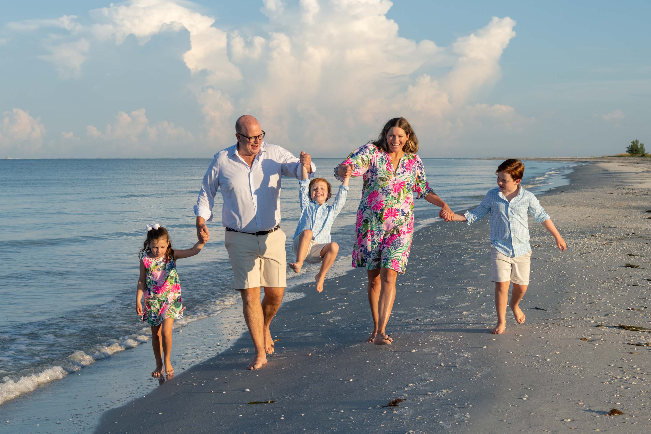 family walking along beach around sunrise swinging their children making them laugh
